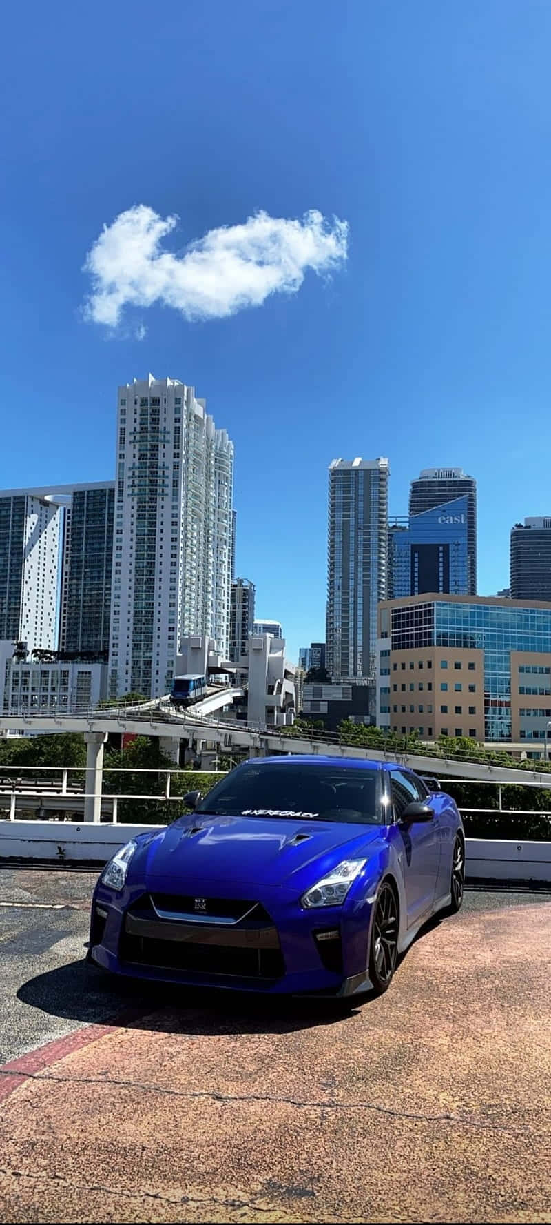 藍色跑車在屋頂上，城市天際線和晴朗天空。 — 吉他 iPhone 壁紙