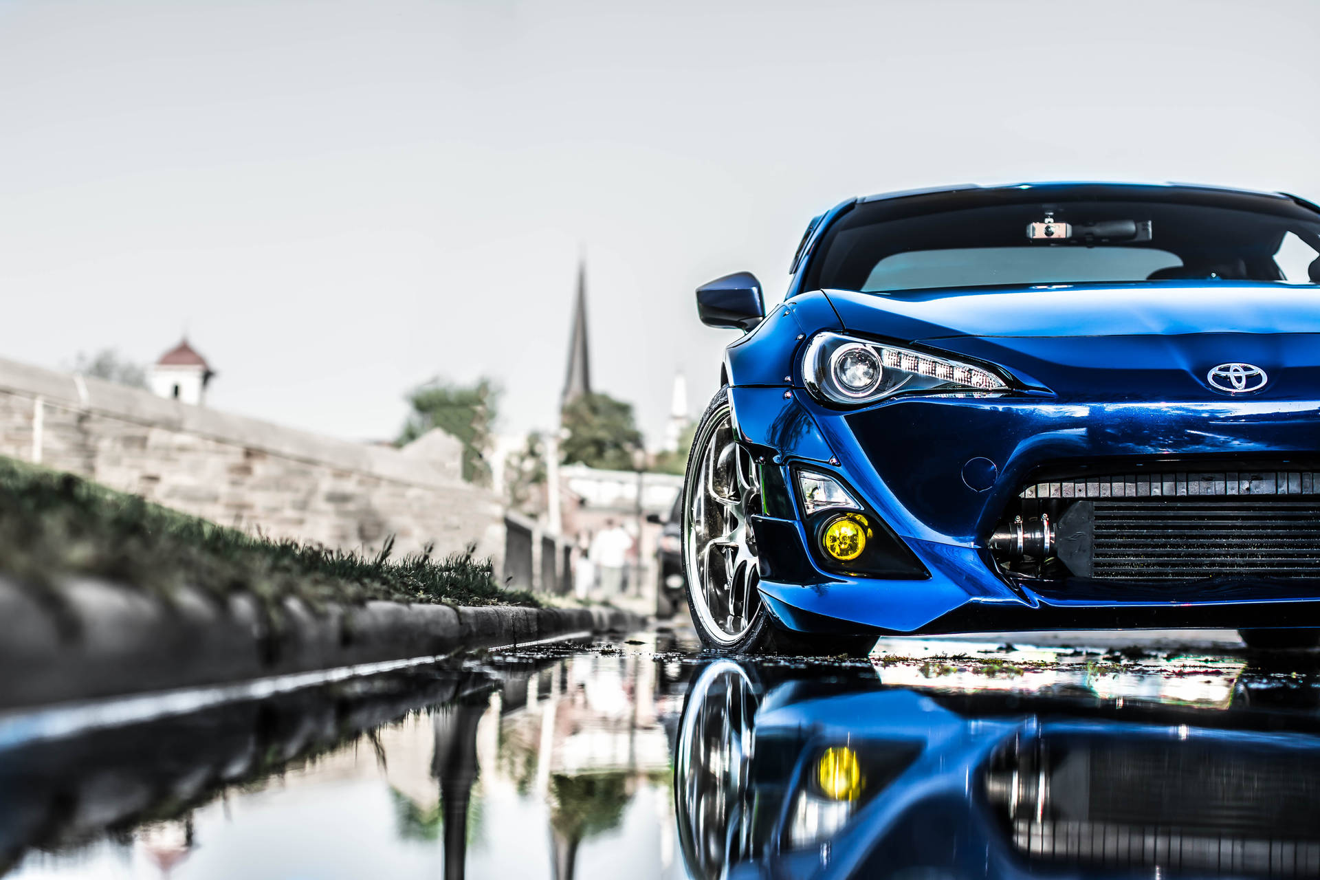 藍色跑車停在潮濕的街道上，水坑中有倒影。 — Toyota Supra 壁紙