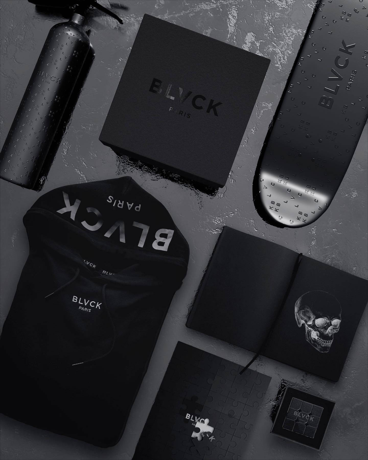 Blvck Paris 桌布 壁紙 — BLVCK PARIS 品牌物品（包括連帽衫、滑板及配件）在潮濕紋理表面上的單色平鋪佈置。