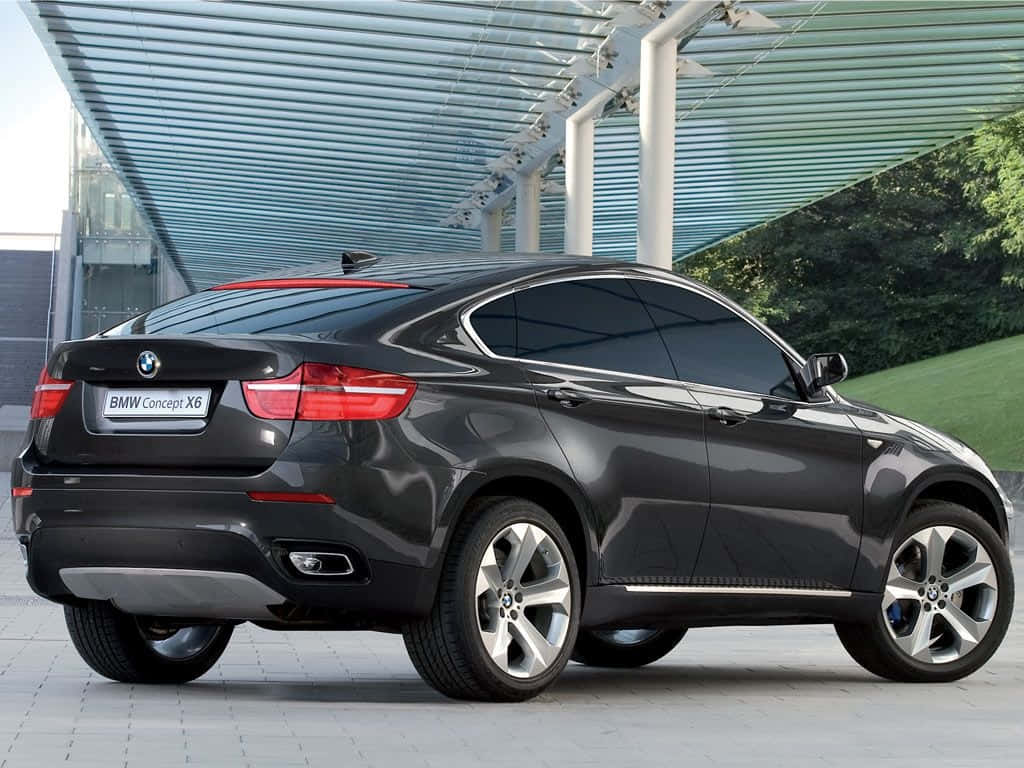 Bmw X6 桌布 壁紙 — 一輛時尚的黑色BMW Concept X6轎跑SUV停放在現代玻璃和鋼製天篷下，背景有綠植。