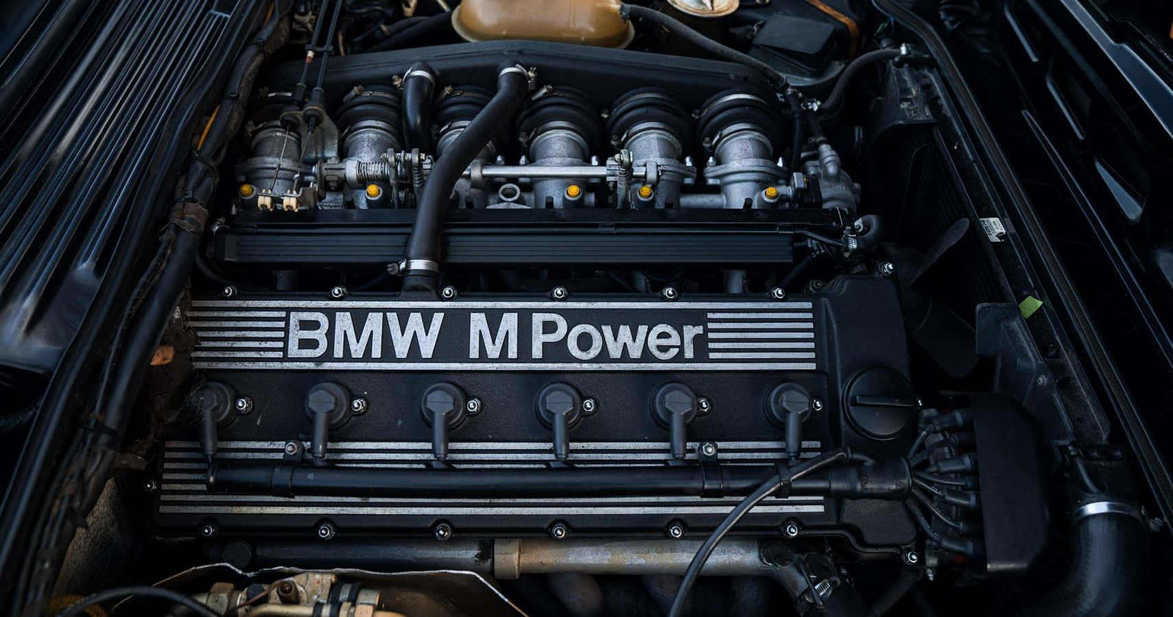 引擎 桌布 壁紙 — BMW M Power 引擎艙特寫，展示引擎蓋燈光下複雜的機械部件和醒目的品牌標識。