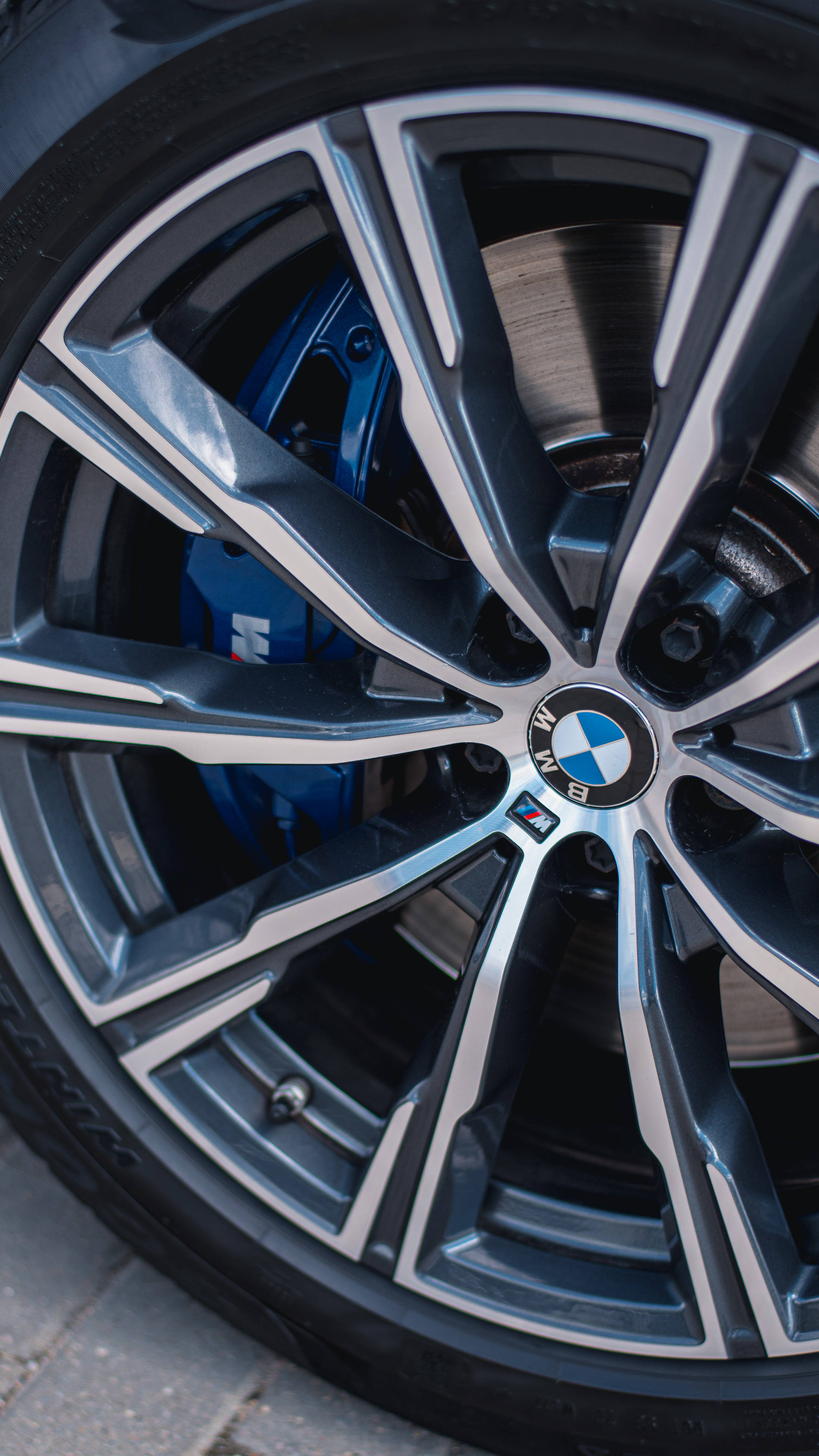 m 桌布 壁紙 — BMW M 型號車輪特寫，展示銀色輪輻、藍色制動卡鉗和路面上的輪胎花紋。
