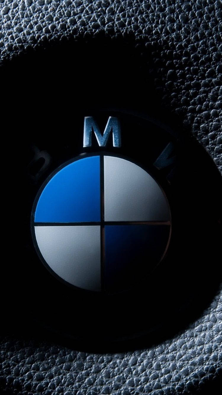 X 桌布 壁紙 — BMW M 標誌在紋理黑色皮革上的特寫，戲劇性的燈光突出了其金屬藍色和銀色象限。