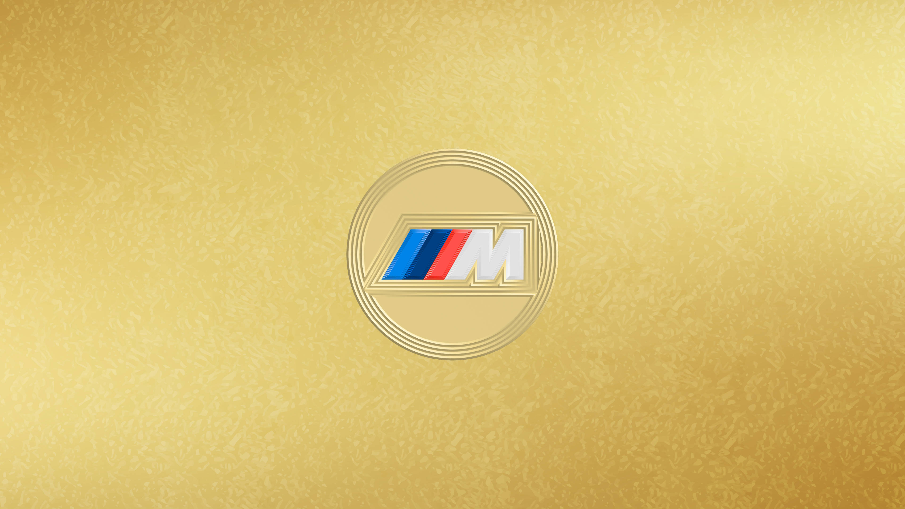BMW 動圖 桌布 壁紙 — BMW M 標誌徽章置於帶有紋理的金色背景中央，帶有微妙的漸變燈光效果。