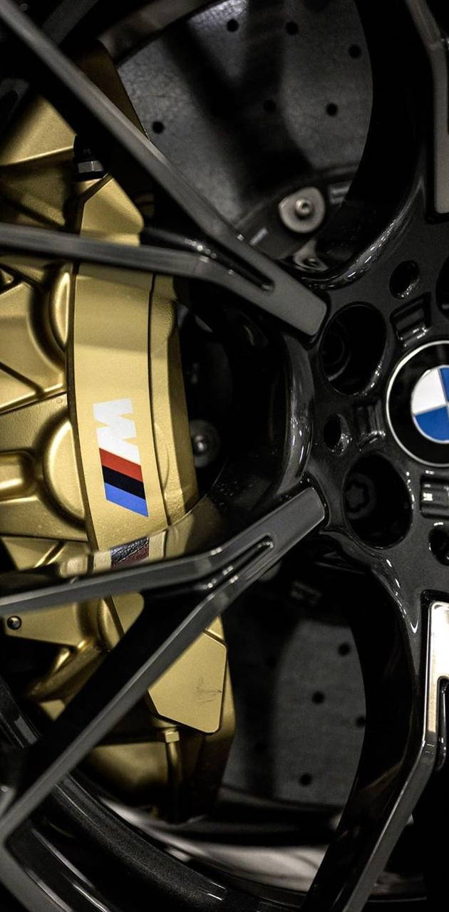 m 桌布 壁紙 — BMW M 汽車金色煞車卡鉗和帶有標誌性標誌的黑色合金輪圈的近距離特寫。