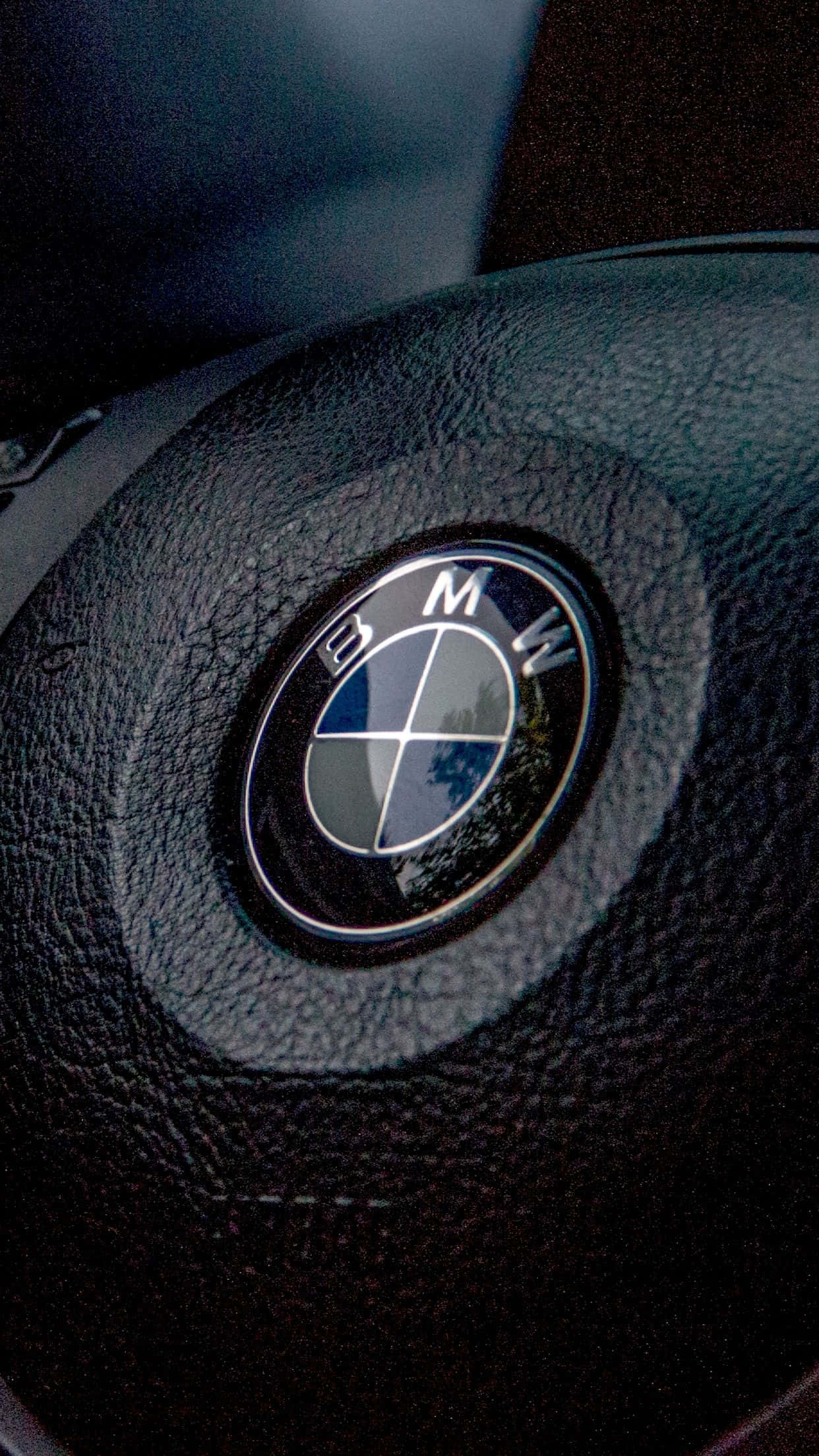 Bmw Logo 桌布 壁紙 — BMW 標誌特寫，位於帶有紋理的黑色皮革方向盤中央，搭配柔和環境燈光。