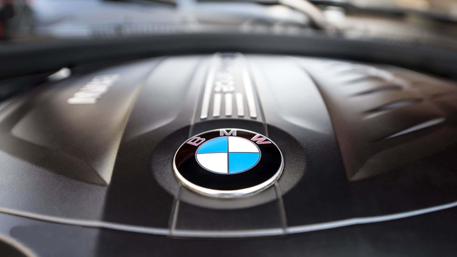 BMW 動圖 桌布 壁紙 — BMW引擎蓋的特寫，帶有標誌性的藍白圓形標誌，位於紋理黑色表面上。