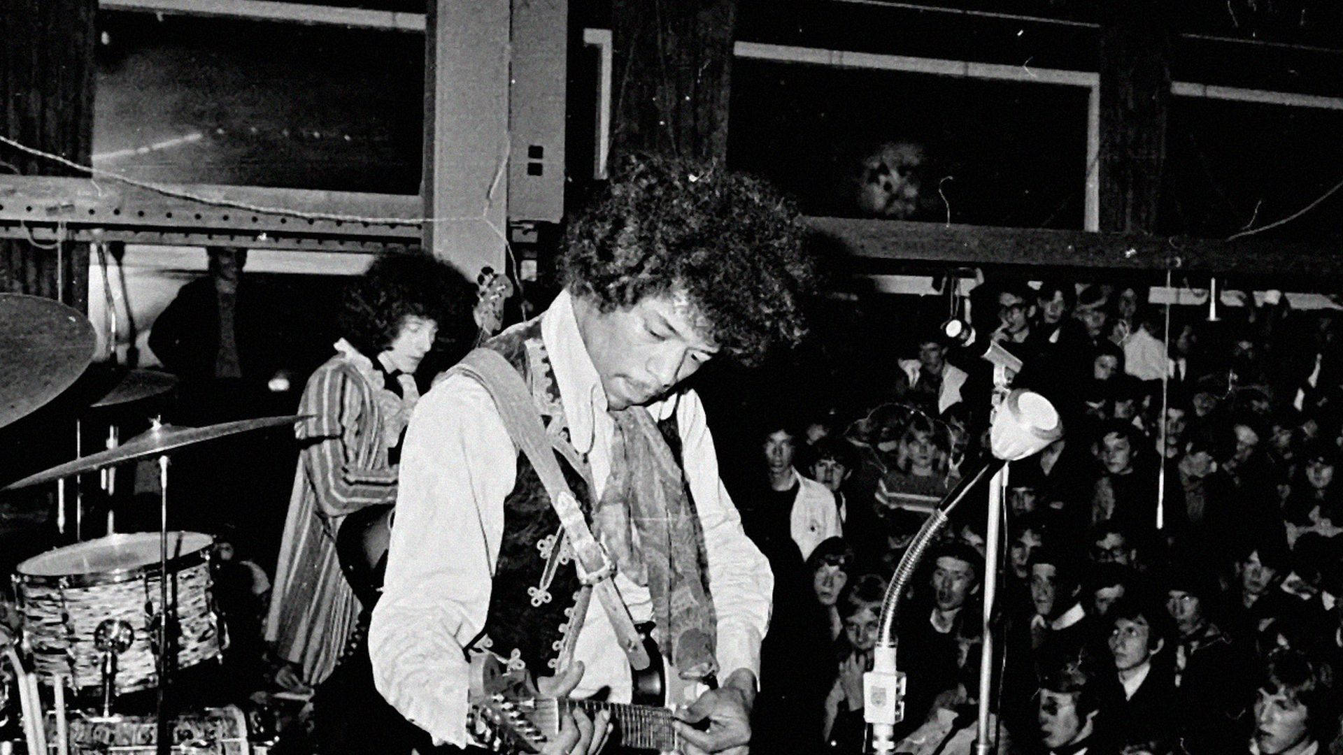 黑白 桌布 壁紙 — Bob Dylan 在昏暗燈光下的復古音樂廳中熱情彈奏吉他，觀眾專注地觀看。