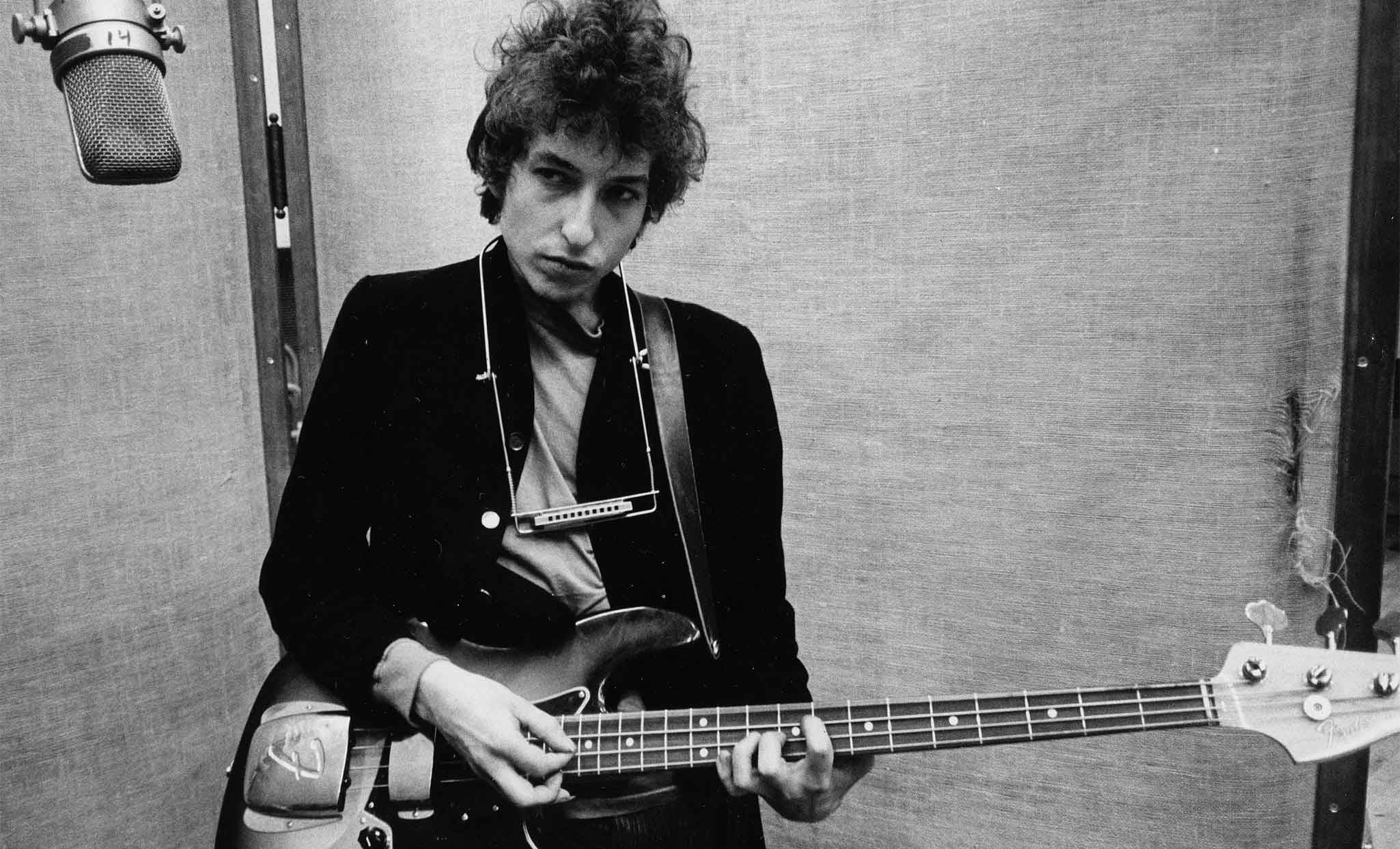 黑白 桌布 壁紙 — Bob Dylan 在錄音室中彈奏低音吉他，背景有復古麥克風和紋理背景。