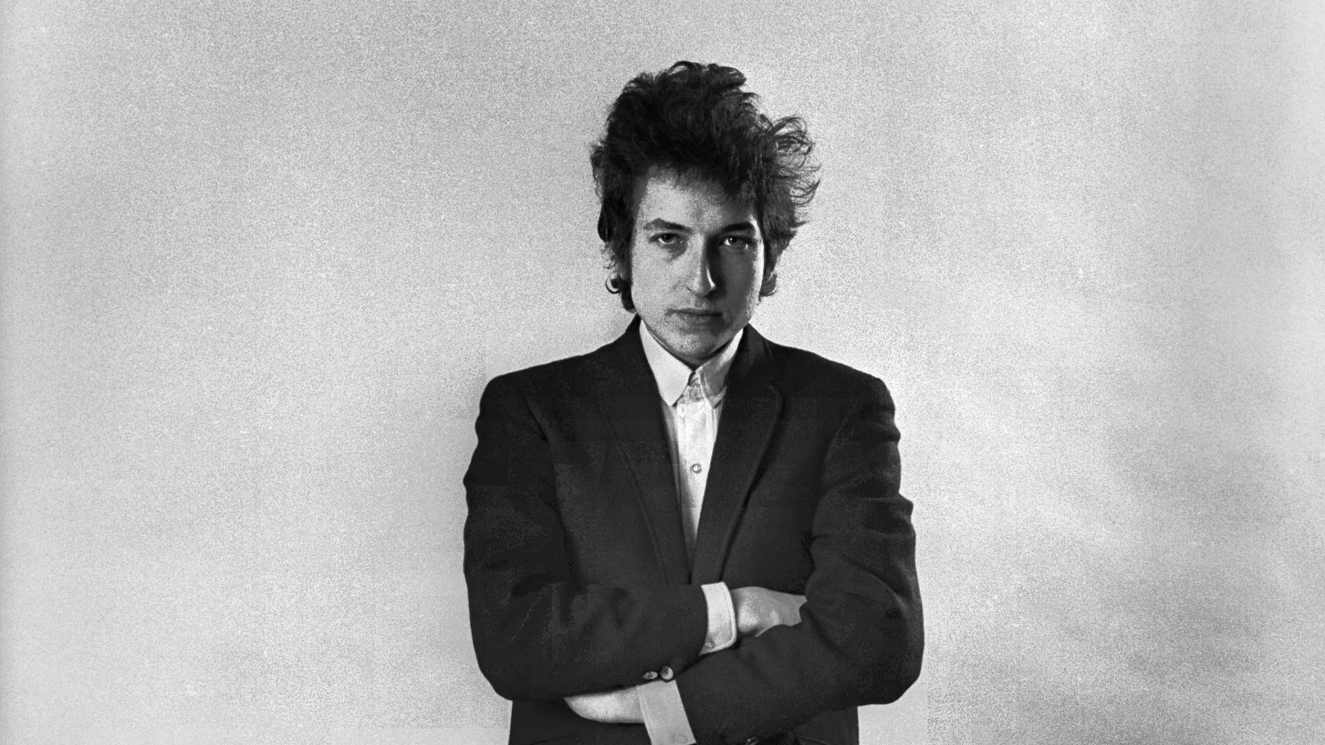 黑白 桌布 壁紙 — Bob Dylan 的黑白肖像，站在有紋理的工作室背景前交叉雙臂。