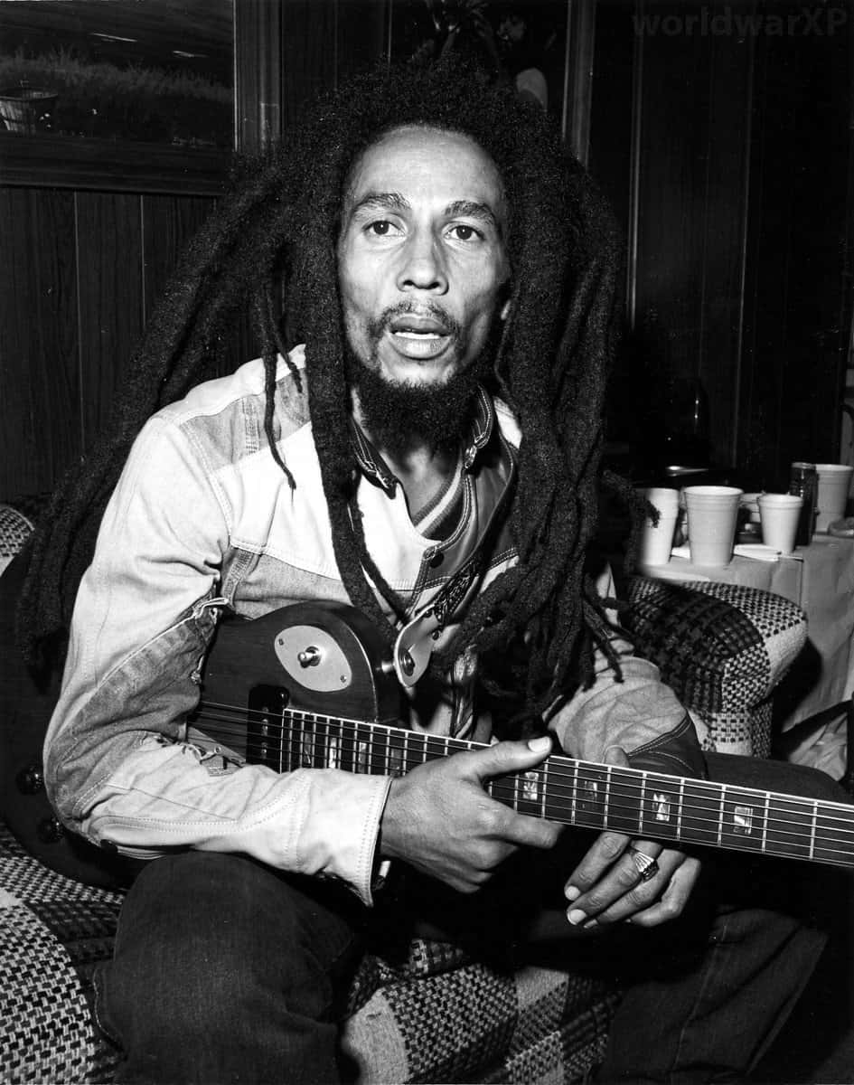Bob Marley 桌布 壁紙 — Bob Marley 坐在昏暗的房間裡拿著吉他，背景有圖案家具和杯子。
