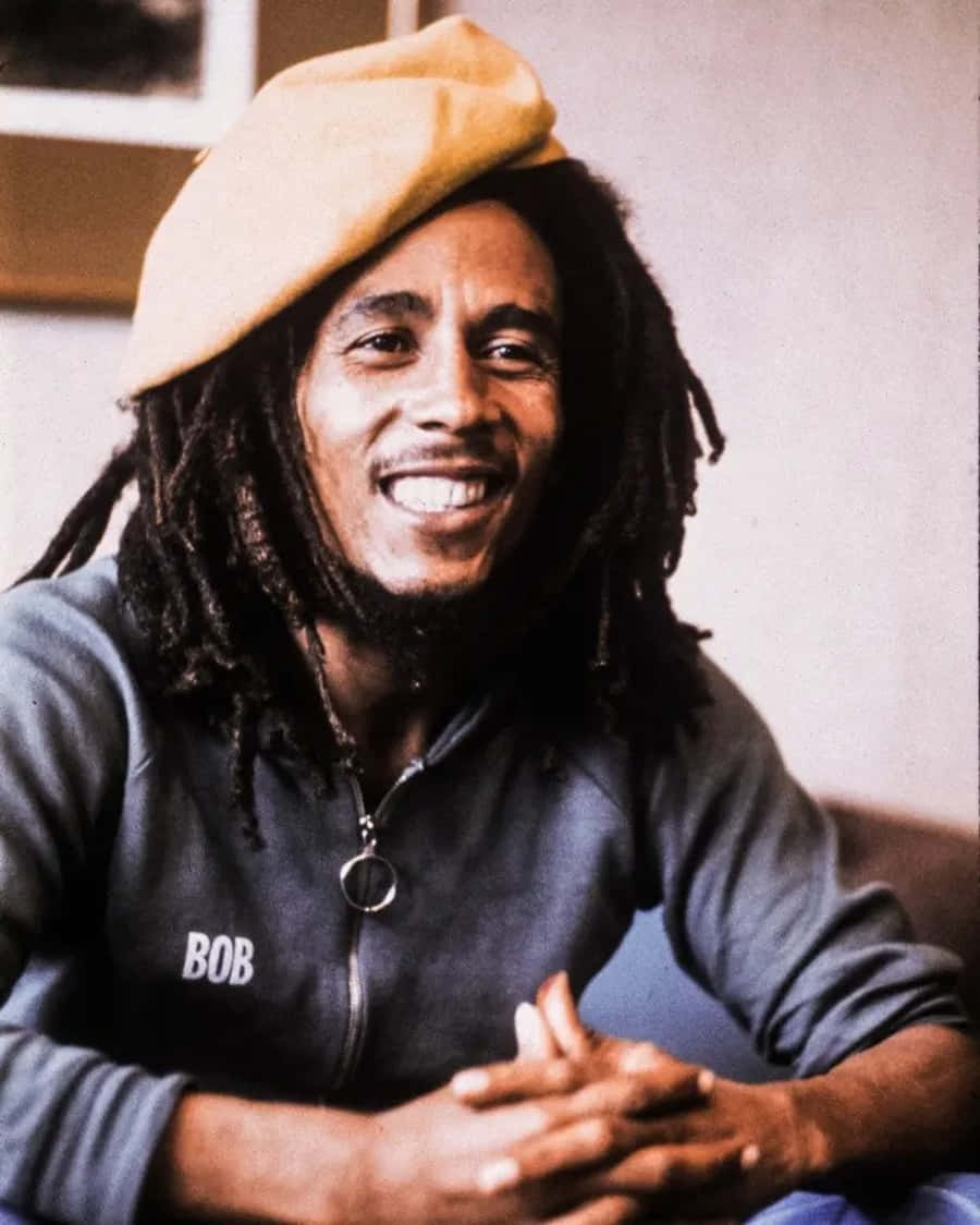 Bob Marley 桌布 壁紙 — Bob Marley 戴著米色貝雷帽和深色連帽衫，胸前繡有他的名字，溫暖地微笑。