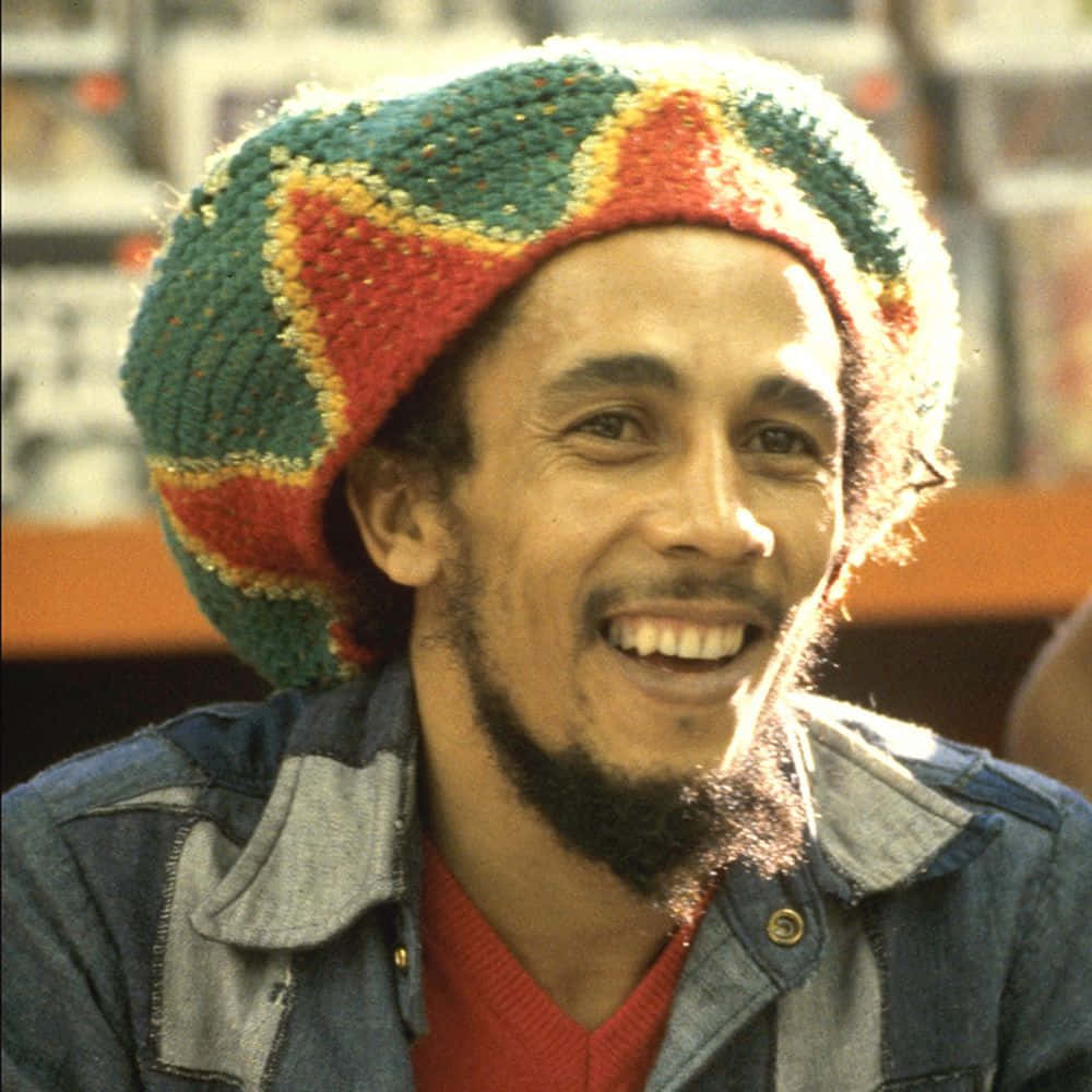 Bob Marley 桌布 壁紙 — Bob Marley 滿懷喜悅，戴著彩色針織帽和牛仔外套，沐浴在溫暖的陽光下。