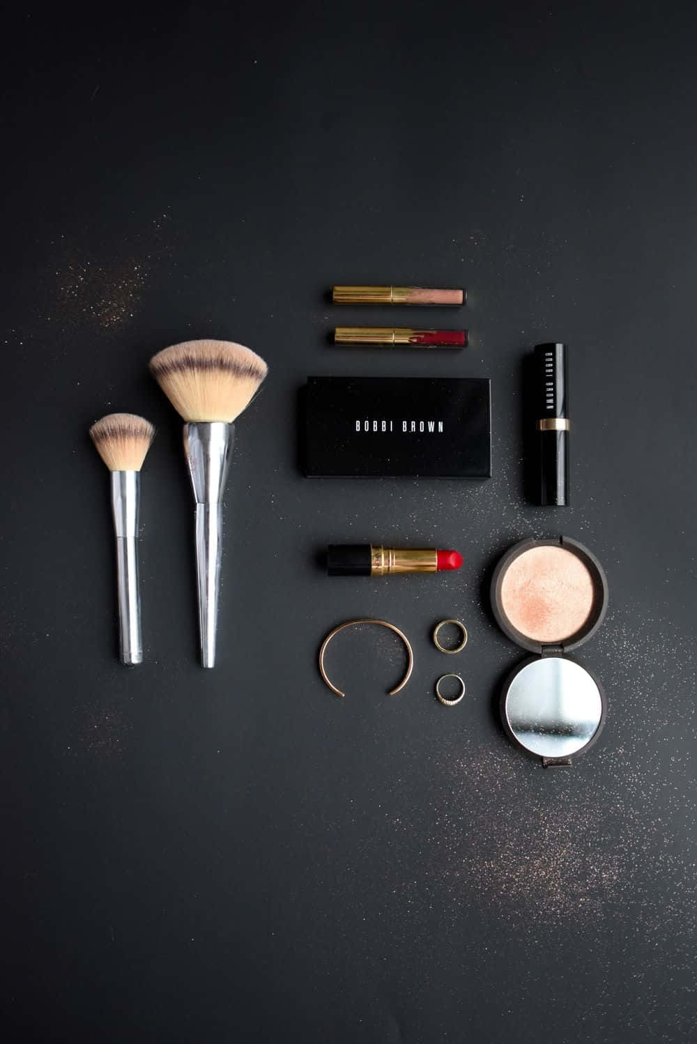 Cute Makeup 桌布 壁紙 — Bobbi Brown 化妝工具和產品以扁平擺放方式排列在深色紋理表面上，並散落著閃粉。