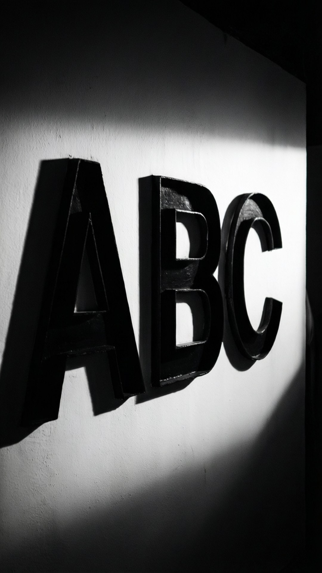 Shadow Play ABC 壁紙 — 大膽的黑色ABC字母在聚焦燈光下，在純白牆壁上投射出戲劇性的陰影。