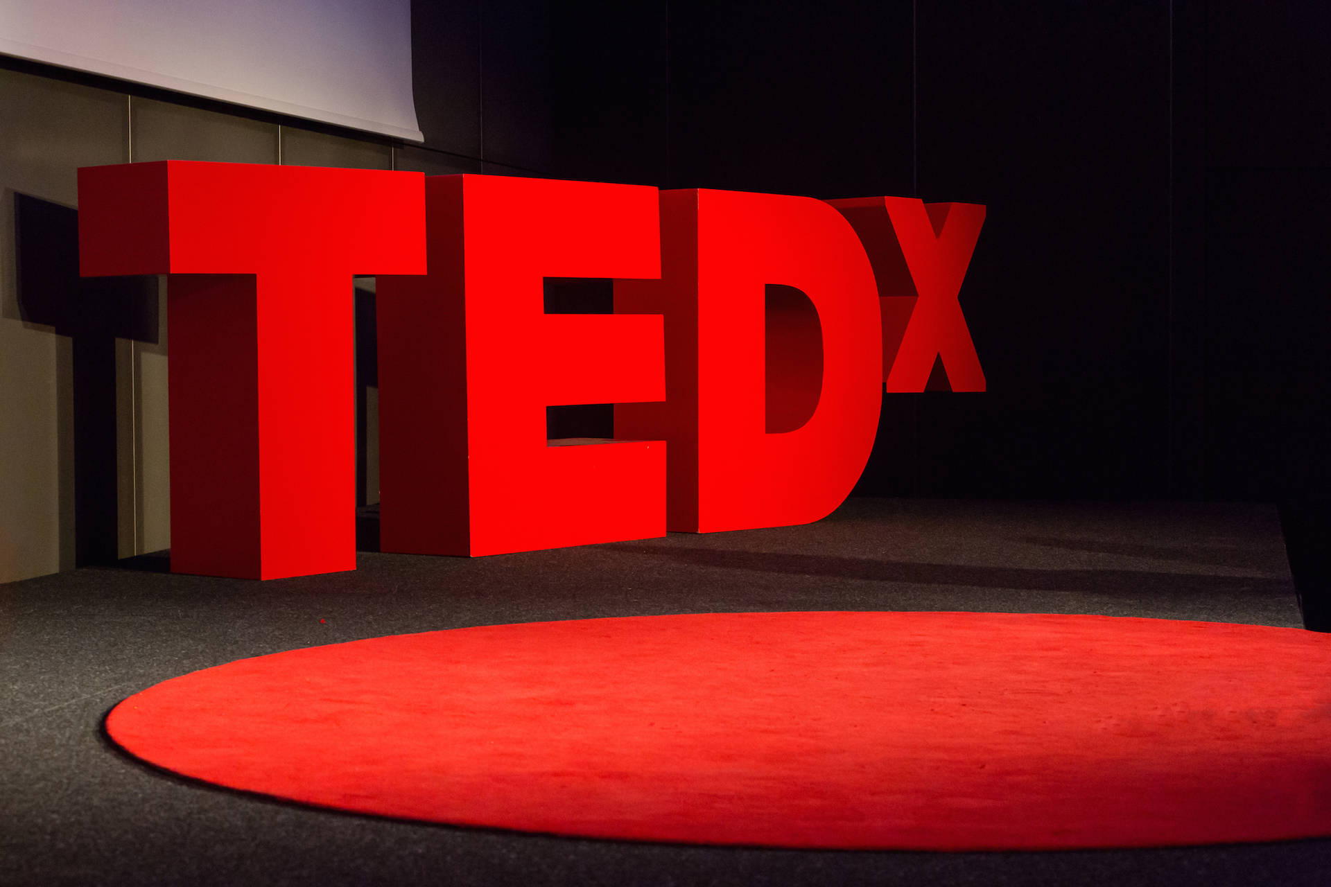 深色舞台上的紅色TEDx字母和圓形地毯。 — 3D 壁紙