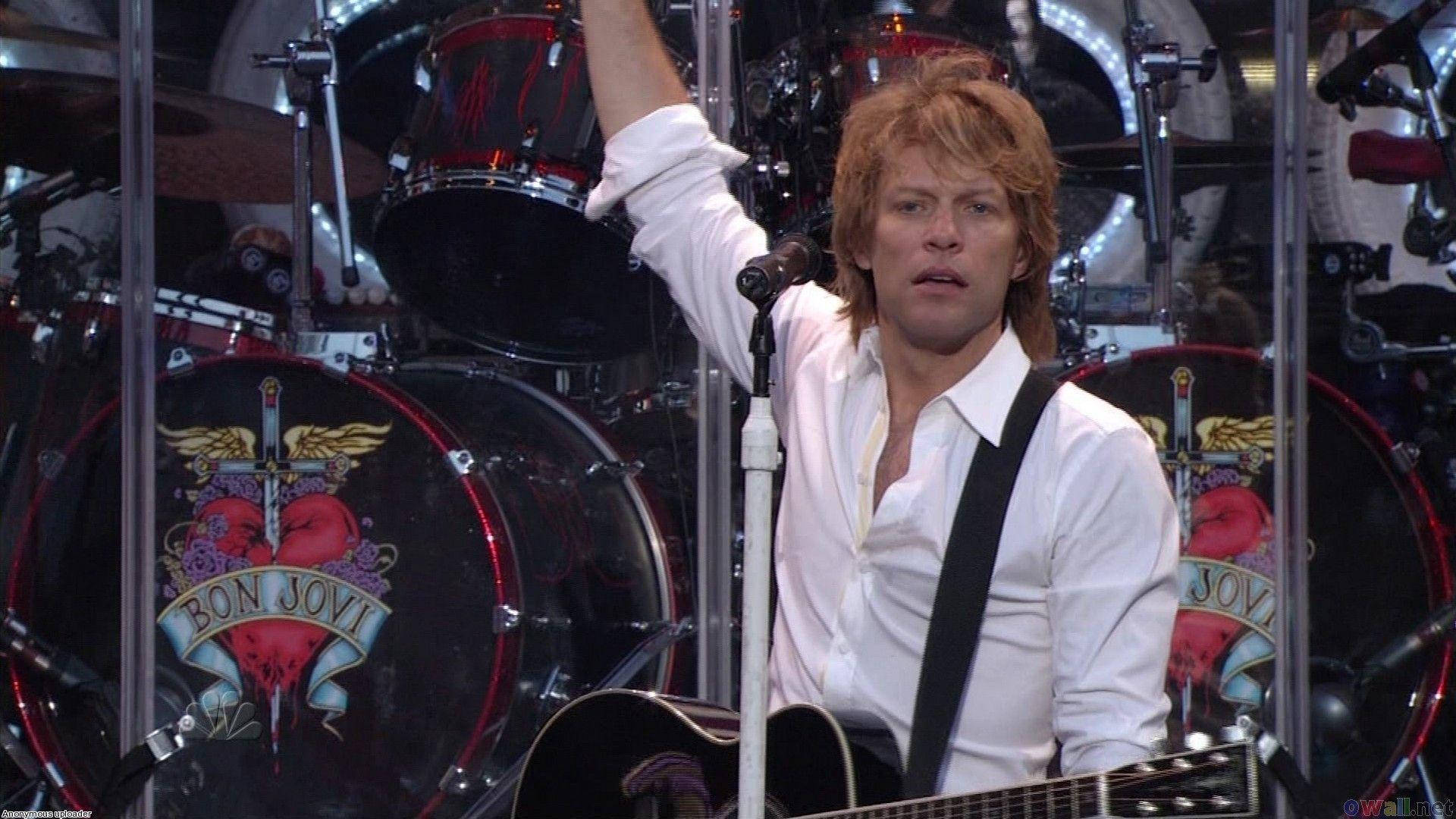 Celebrity 桌布 壁紙 — Bon Jovi 在舞台上充滿活力地表演，配備吉他和鼓組，上面有他標誌性的心形和劍標誌。