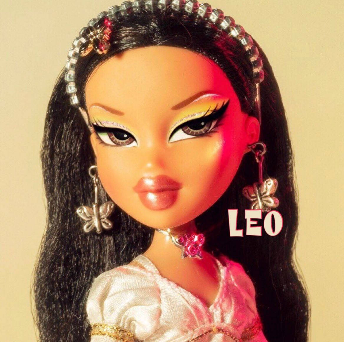 Bratz 桌布 壁紙 — Bratz 公仔特寫，長黑髮，戴珠寶頭帶、蝴蝶耳環和粉紅色連衣裙，在溫暖燈光下。