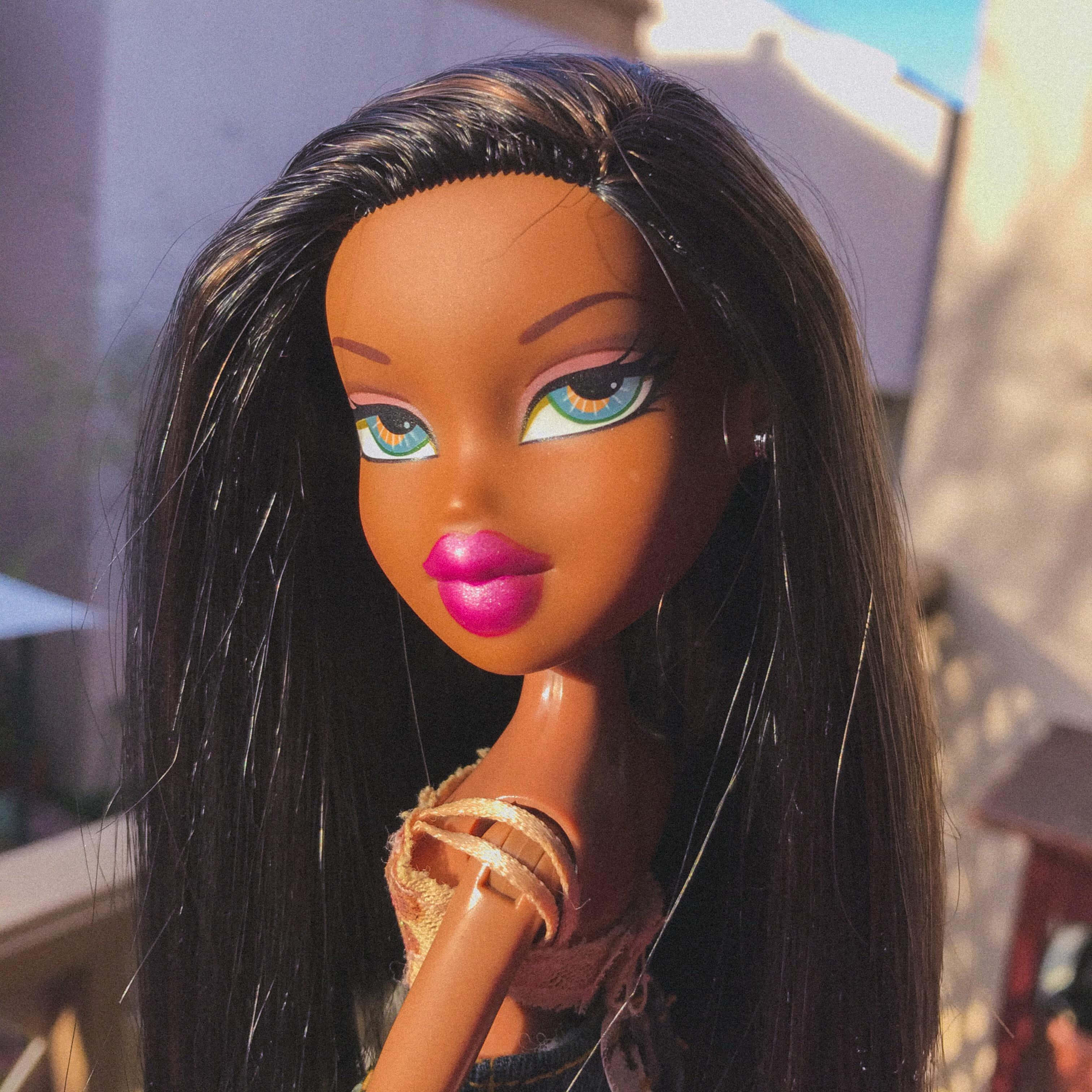 bratz 美學 桌布 壁紙 — Bratz 娃娃的特寫，長長的黑髮、亮粉紅色的嘴唇和引人注目的藍色眼睛，沐浴在溫暖的陽光下。
