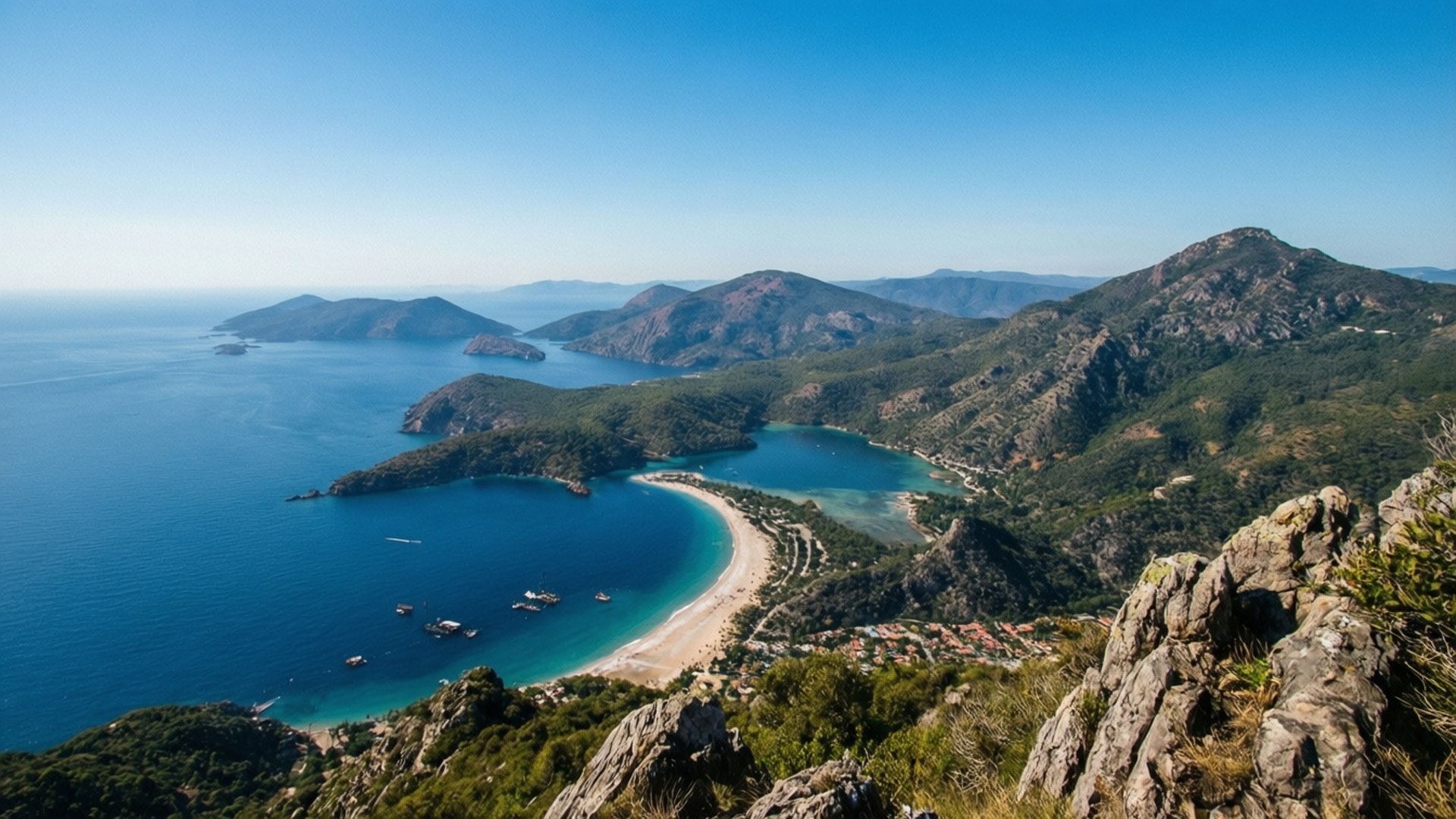 Yara Archipelago Panorama 壁紙 — 在清澈的藍天下，一個令人嘆為觀止的鳥瞰圖，展現了坐落在崎嶇綠色山脈之間的碧綠海灣。