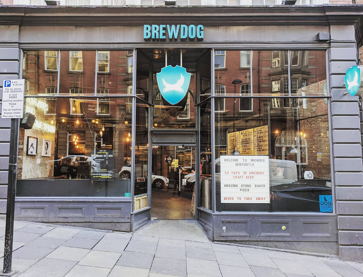 Drink 桌布 壁紙 — BrewDog 啤酒廠店面，大型玻璃窗反射磚建築和街道標誌，在日光下。