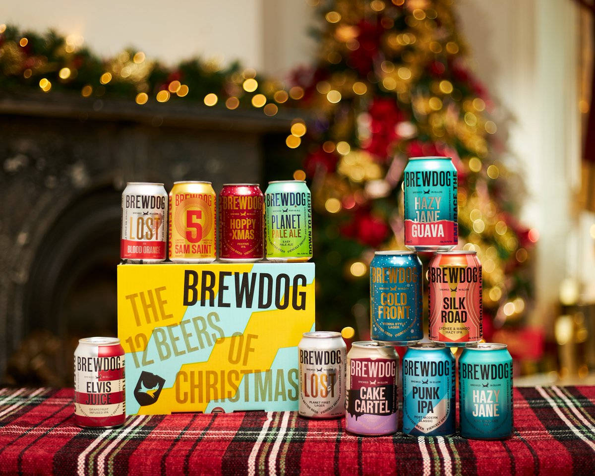Drink 桌布 壁紙 — BrewDog 的 12 Beers of Christmas 罐裝啤酒在裝飾好的聖誕樹和壁爐前的格子毯上擺放的節日展示。