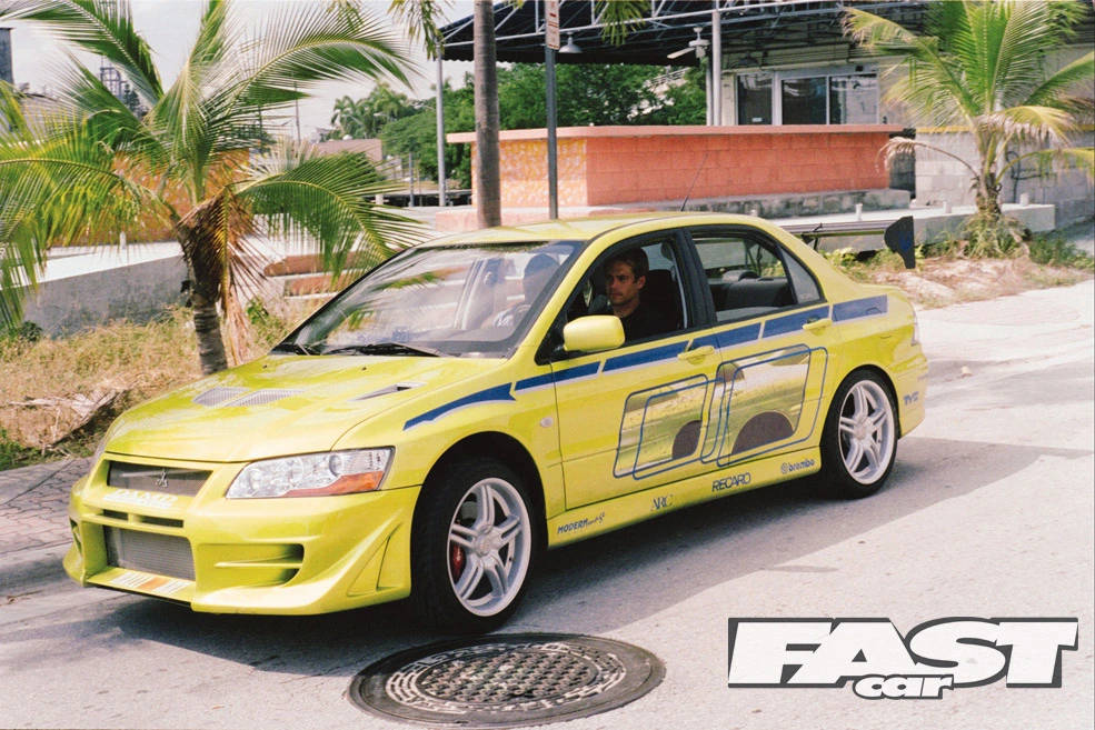 一輛黃色改裝跑車停在熱帶街道上，有棕櫚樹。 — 保羅·沃克汽車 壁紙