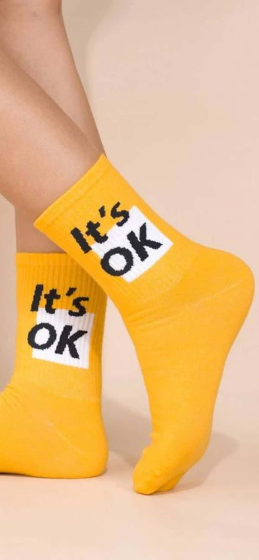  壁紙 — 鮮黃色襪子，在柔軟的米色背景上印有粗體黑色文字「It's OK」。