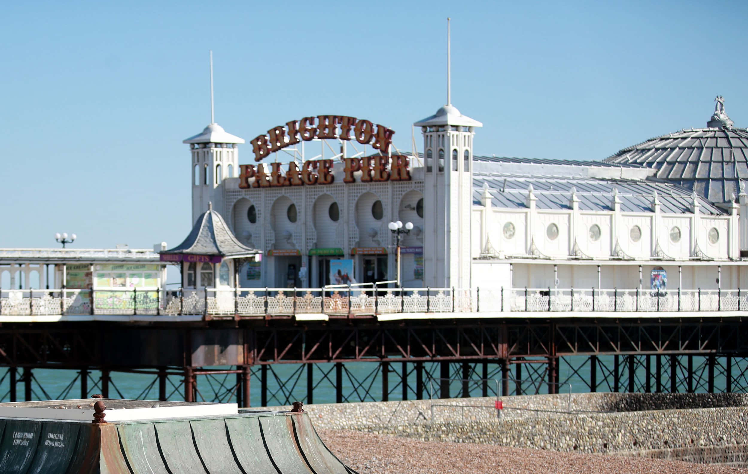 Brighton Pier 桌布 壁紙 — Brighton Palace Pier 在清澈藍天下延伸至碧綠色的海面，擁有白色建築和標誌性招牌。