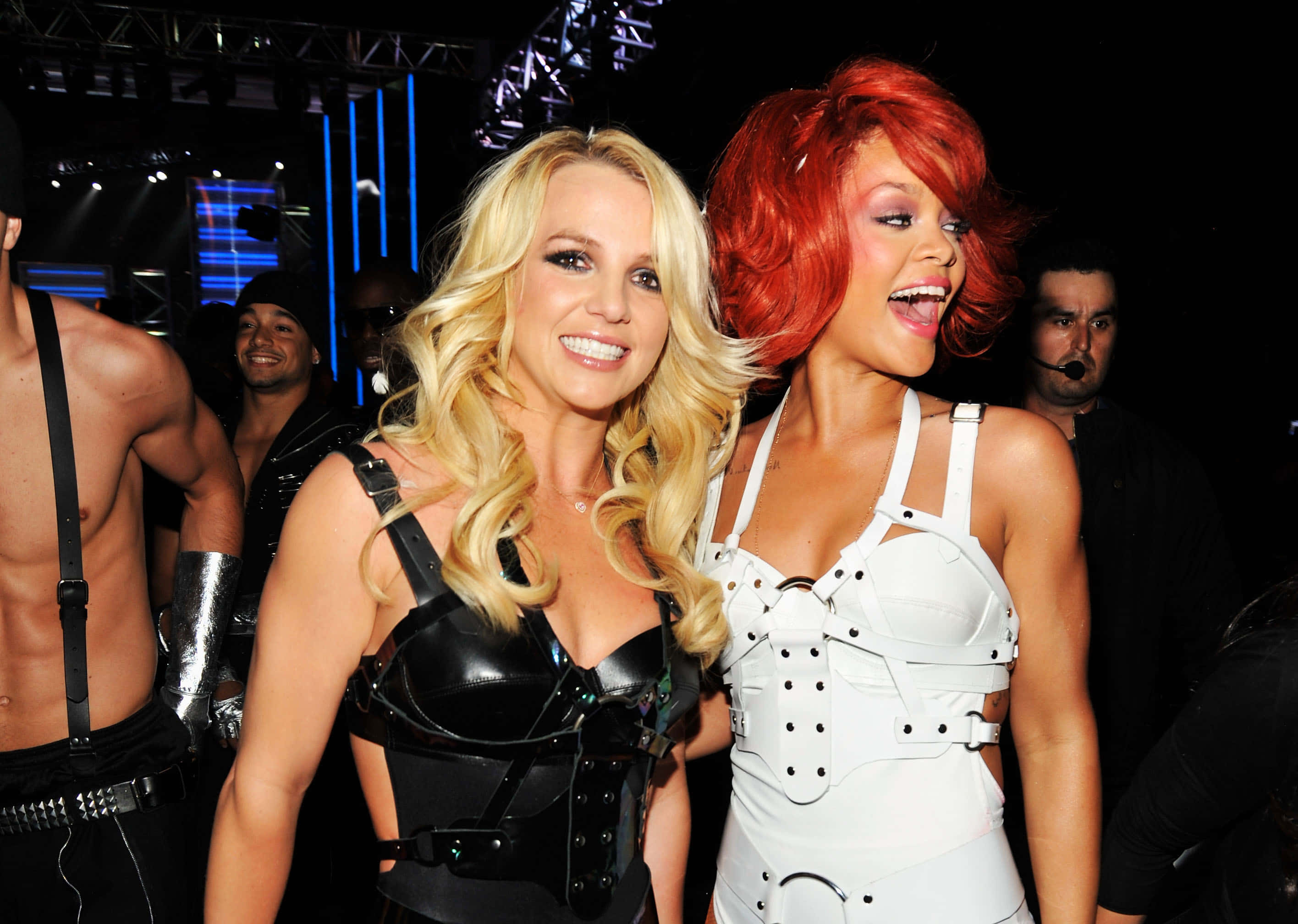 Britney Spears 桌布 壁紙 — Britney Spears 和 Rihanna 在明亮的演唱會燈光下，以深色背景穿著大膽的舞台服裝一起擺姿勢。