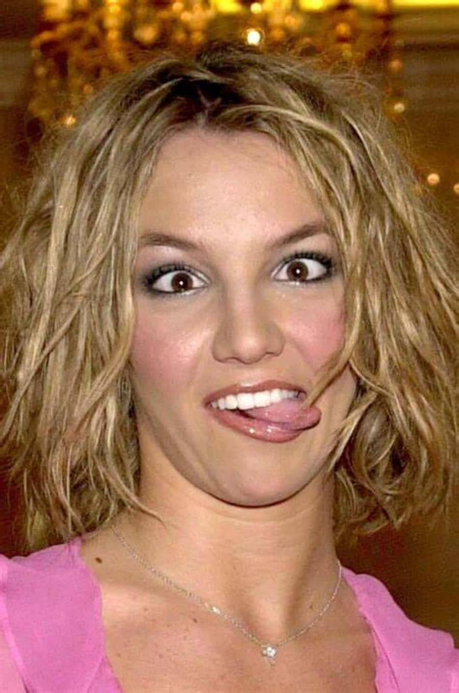 搞笑 桌布 壁紙 — Britney Spears 在金色吊燈背景下伸出舌頭，露出頑皮笑容。