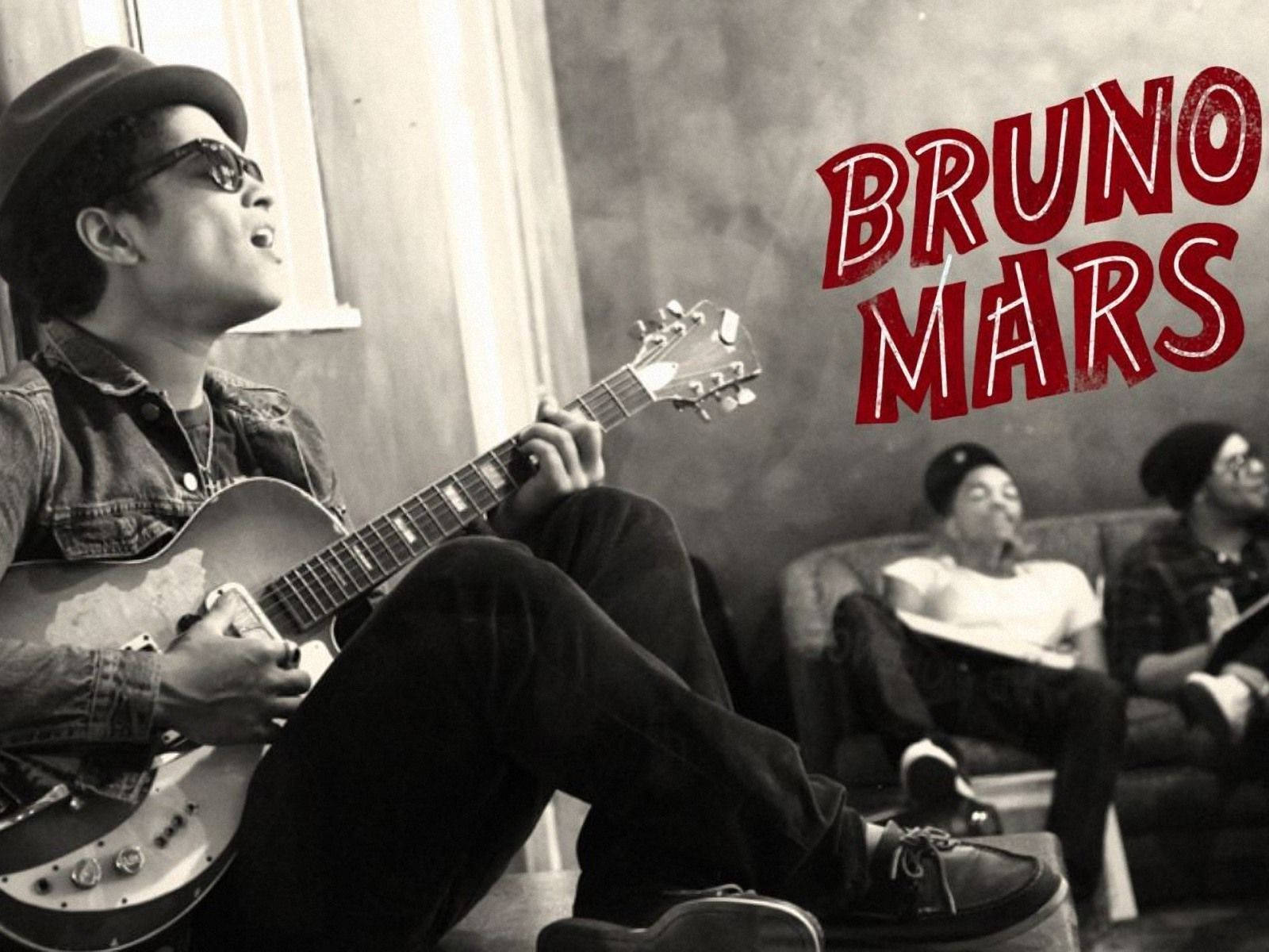 Bruno Mars 桌布 壁紙 — Bruno Mars 以黑白風格彈奏電吉他，紅色文字覆蓋，兩位樂隊成員在背景中放鬆。