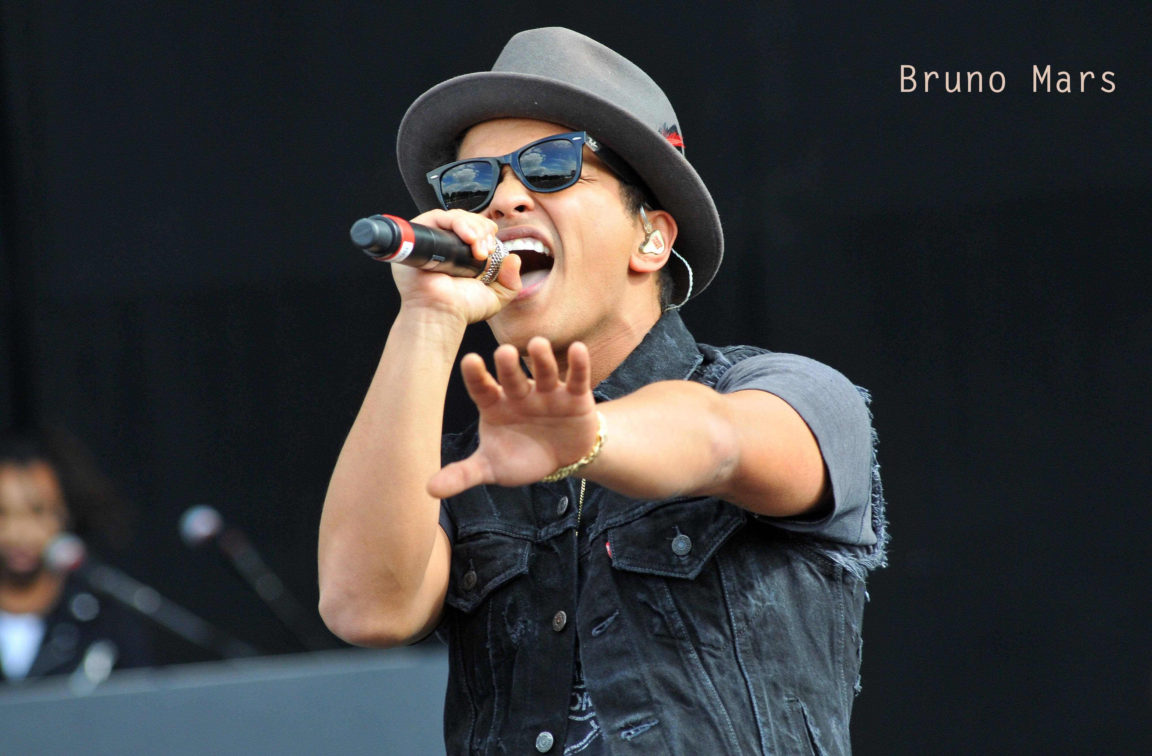 Bruno Mars 桌布 壁紙 — Bruno Mars 戴著紳士帽、太陽眼鏡和牛仔背心，在舞台上深情地對著麥克風唱歌。
