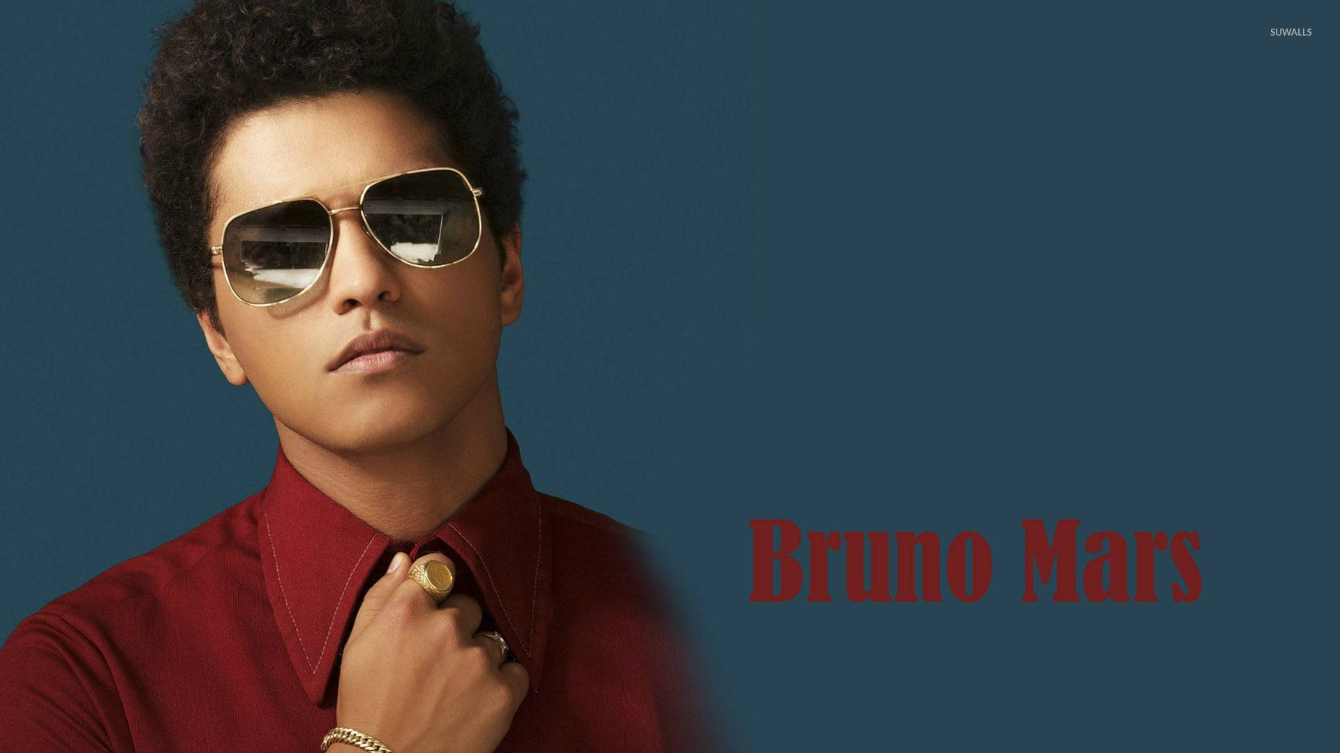 Bruno Mars 桌布 壁紙 — Bruno Mars 戴著飛行員太陽眼鏡和紅色襯衫，在深藍色背景前調整衣領。