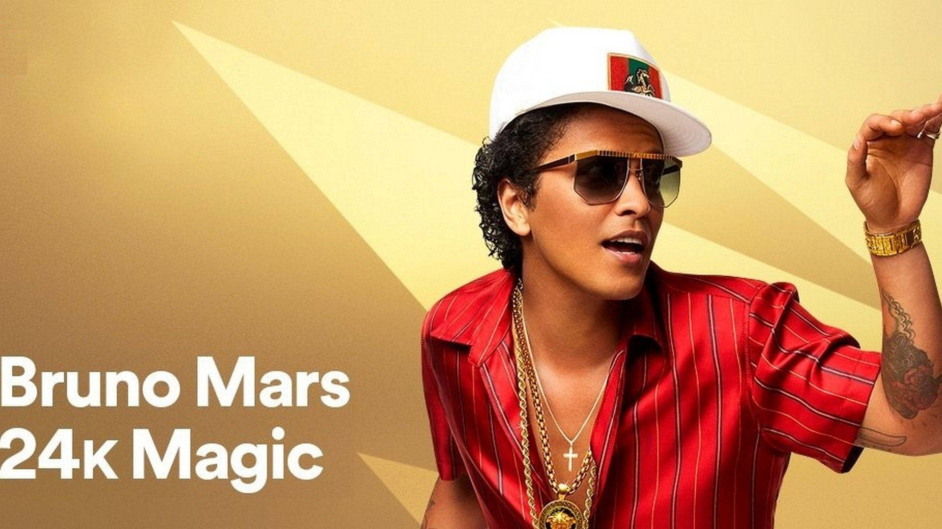 火星人布魯諾 桌布 壁紙 — Bruno Mars 穿著紅色細條紋襯衫和白色帽子，在金色幾何背景前自信地擺姿勢。