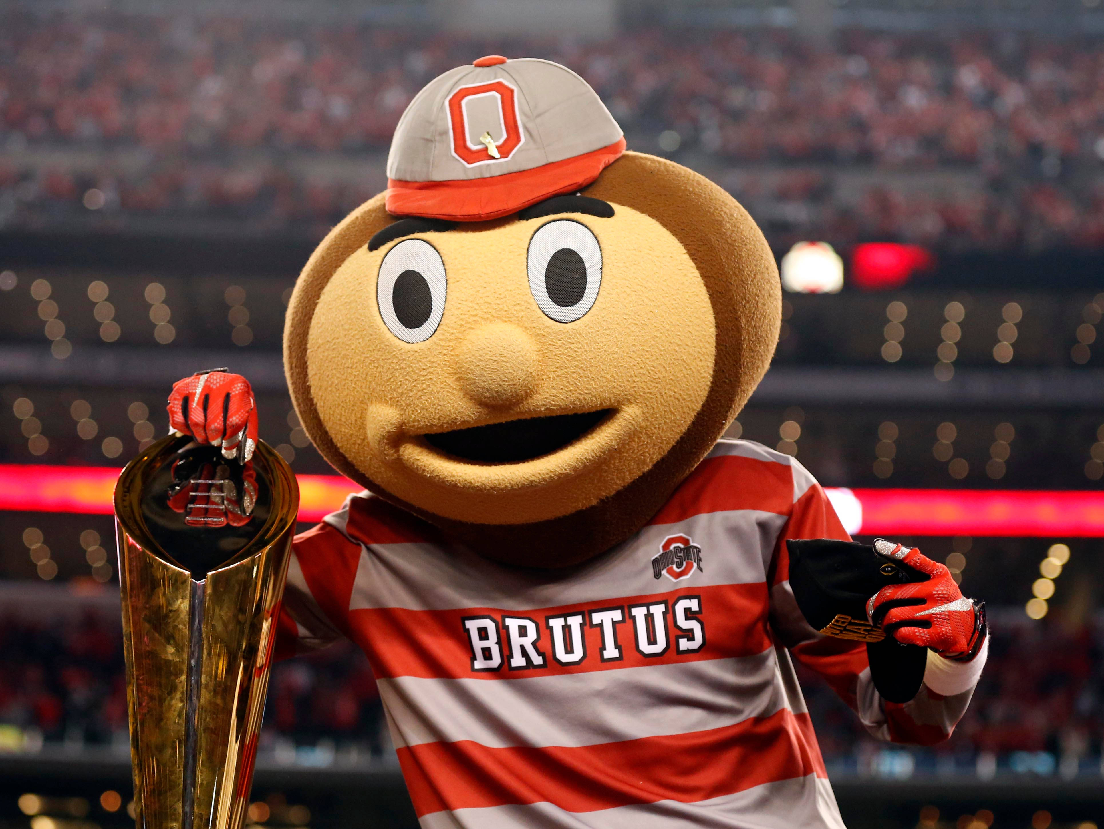 college 桌布 壁紙 — Brutus Buckeye 吉祥物身穿紅灰條紋球衣，在擠滿歡呼球迷的體育館中自豪地高舉閃閃發光的金色獎盃。