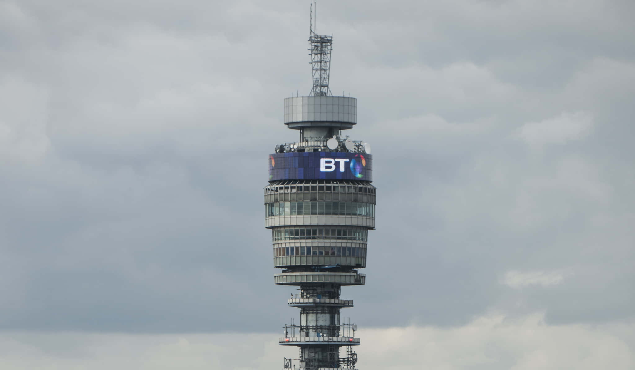 tower 桌布 壁紙 — BT Tower 高聳入雲，其標誌性的圓柱結構和發光的藍色BT標誌在陰天背景下格外醒目。