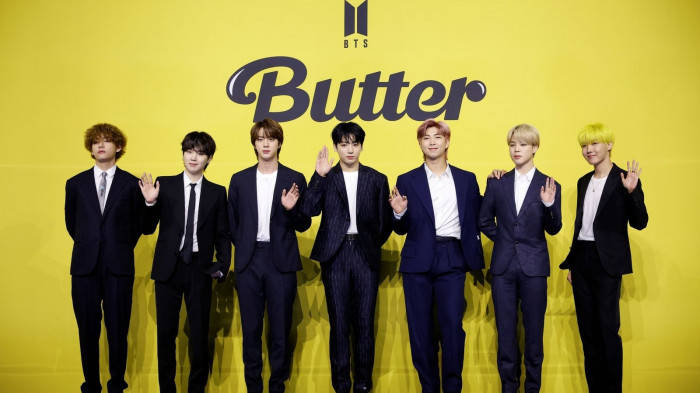 七名穿西裝的男子在黃色牆前揮手，上有 Butter 文字。 — Bts 壁紙