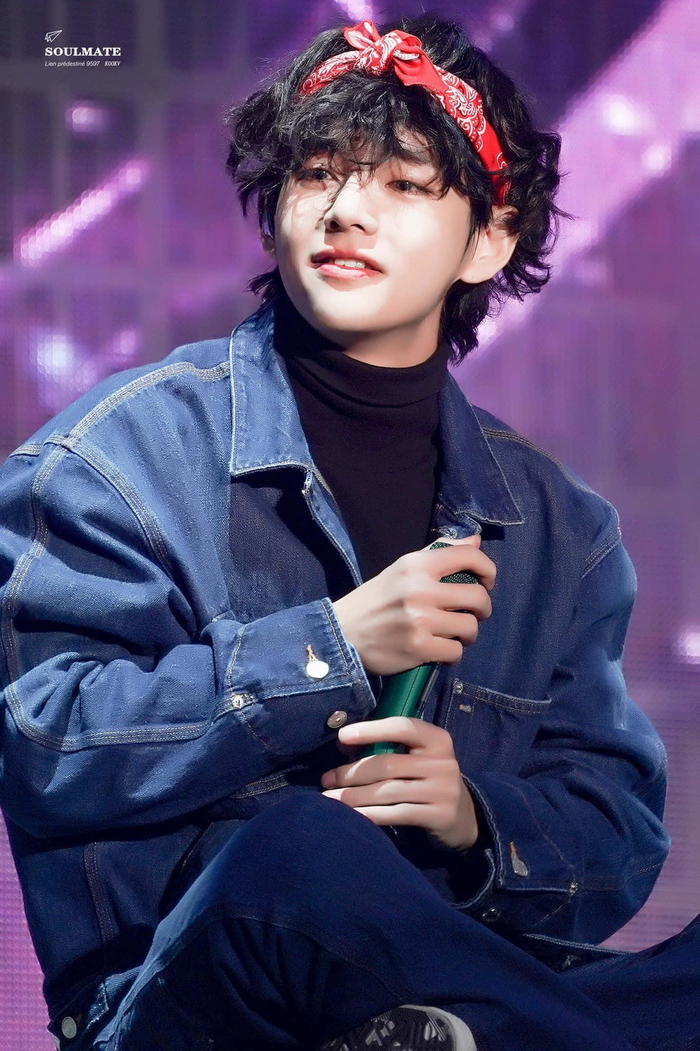 BTS 的 V——可愛的力量 壁紙 — 一位年輕男子，捲髮、戴紅色頭巾，在紫色燈光的舞台上微笑著拿著麥克風。