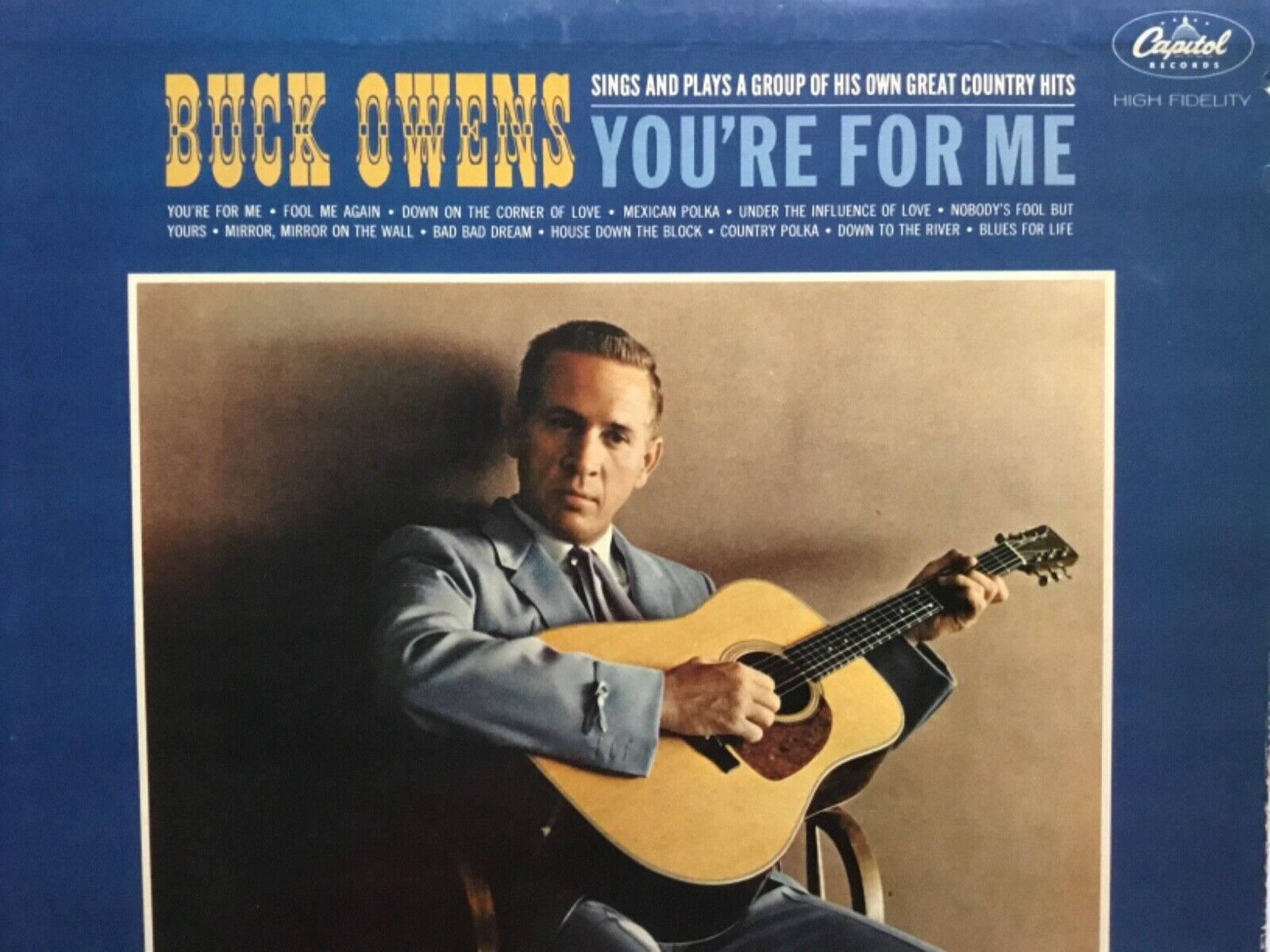 Celebrity 桌布 壁紙 — Buck Owens 身穿西裝，在溫暖的米色背景下，手持原聲吉他，出現在復古 Capitol Records 專輯封面上。