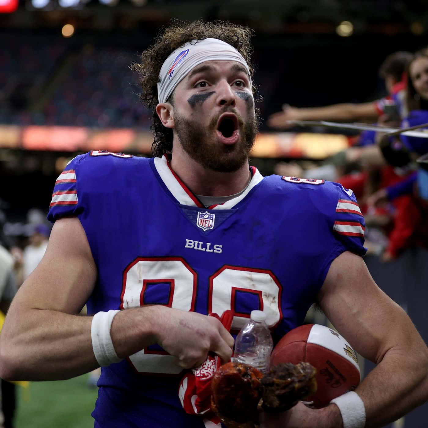  壁紙 — 一名身穿藍色球衣的 Buffalo Bills 美式足球員在球場燈光下，拿著美式足球和雞翅慶祝。