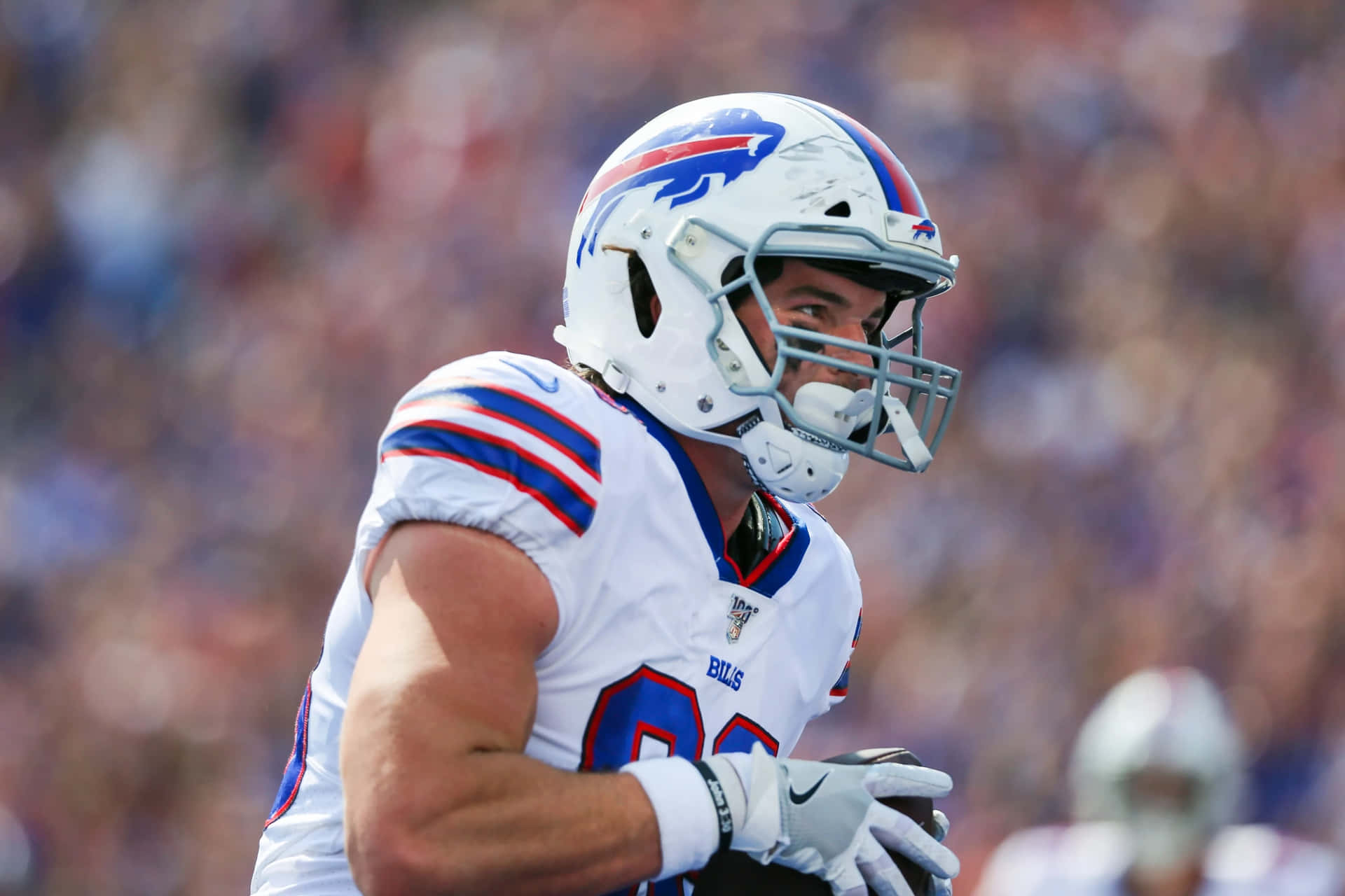  壁紙 — 一名身穿白色、藍色和紅色球衣的 Buffalo Bills 足球員在日間比賽中顯得專注，背景是模糊的體育場人群。