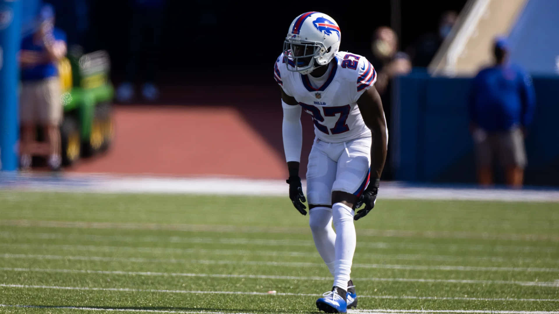  壁紙 — 一名身穿白色球衣的 Buffalo Bills 美式足球員在陽光明媚的綠色球場上行走，背景是模糊的體育場。