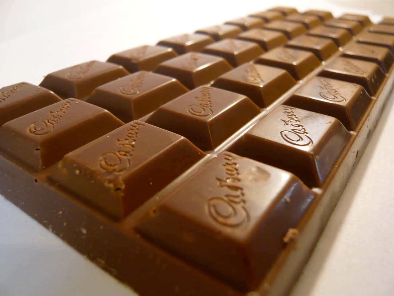 Brown Chocolate 桌布 壁紙 — Cadbury 巧克力棒的近距離特寫，白色表面上帶有光澤的棕色方塊，上面壓印了品牌名稱。