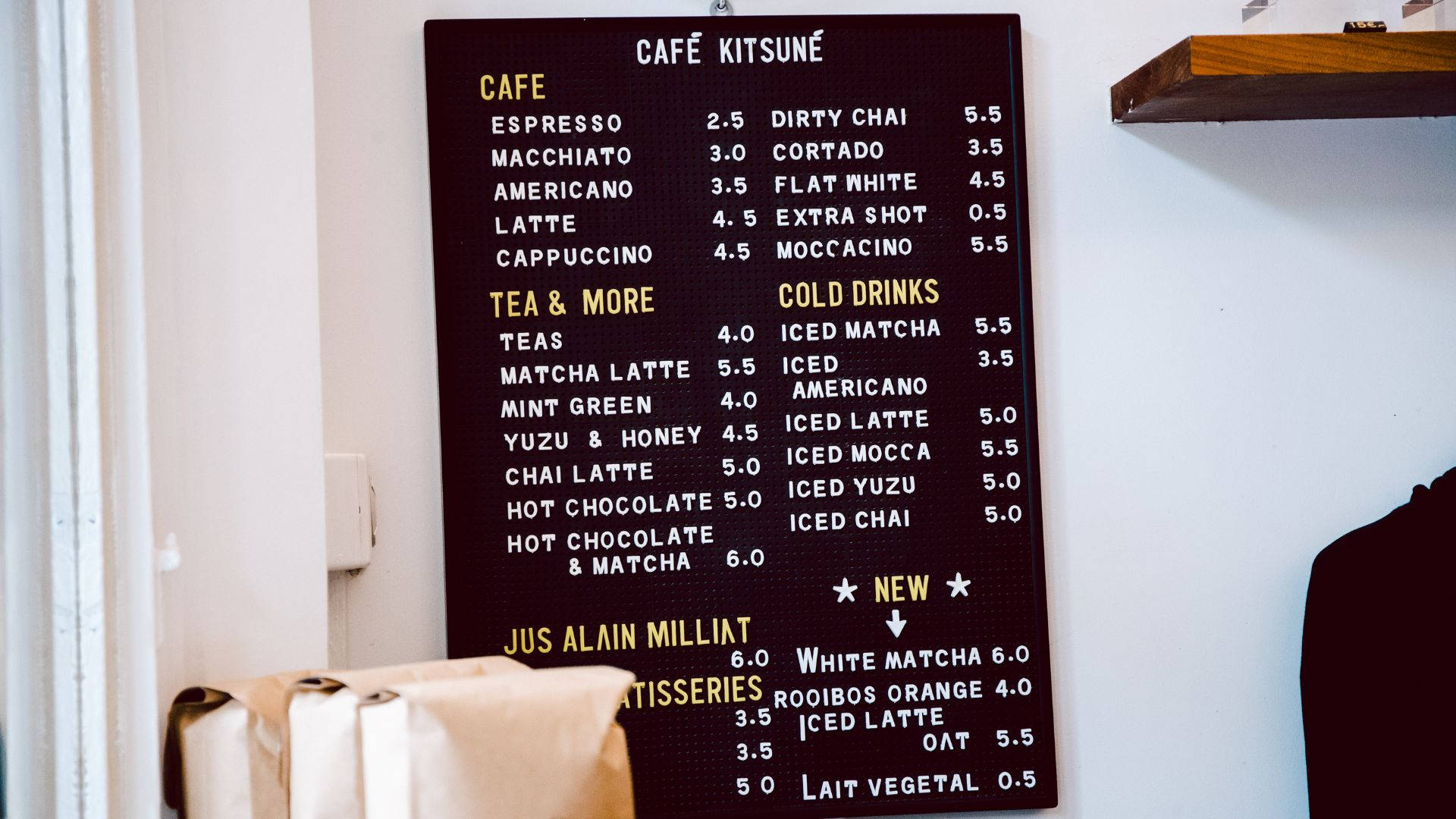 美學 桌布 壁紙 — Café Kitsuné 的深色木製菜單板列出咖啡、茶和冷飲的價格，營造舒適的咖啡館環境。