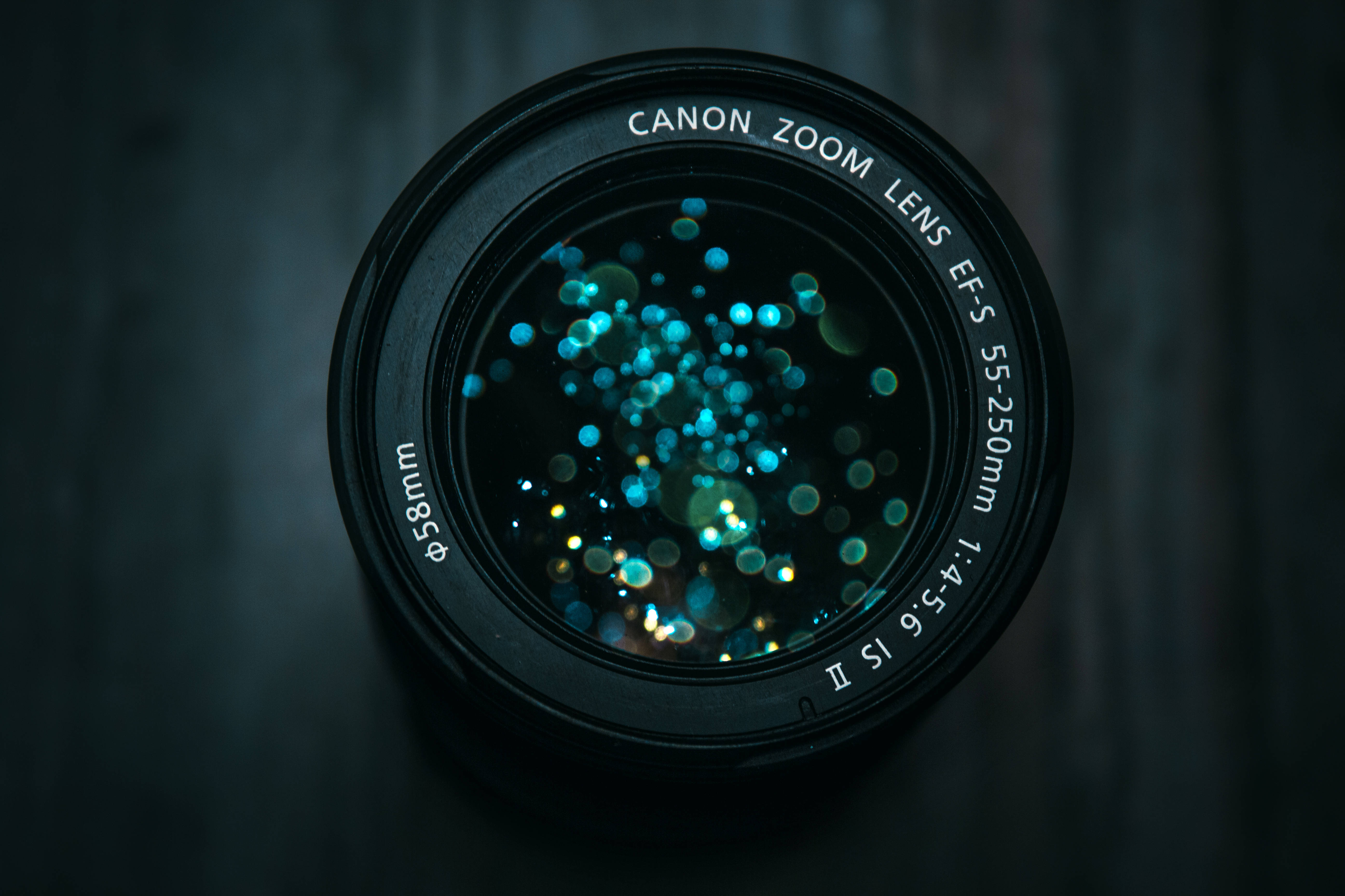 攝影 桌布 壁紙 — Canon相機鏡頭的近距離特寫，鏡頭玻璃反射出藍色和綠色的散景光，背景為深色木質。