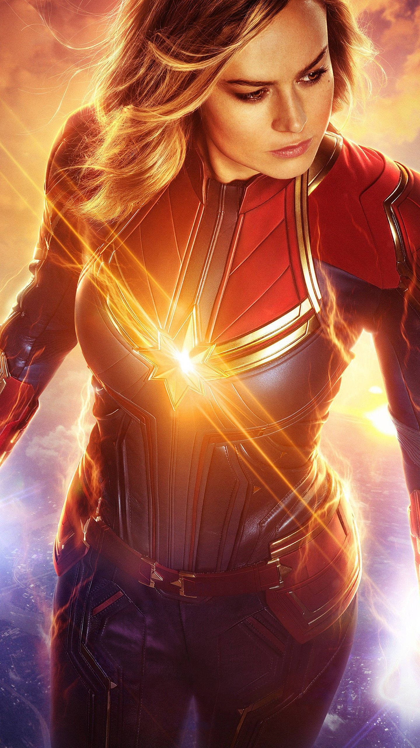 captain marvel iPhone 桌布 壁紙 — Captain Marvel 強勢地站立，身穿發光的紅藍戰衣，胸前散發出耀眼的星爆，背景是宇宙天空。