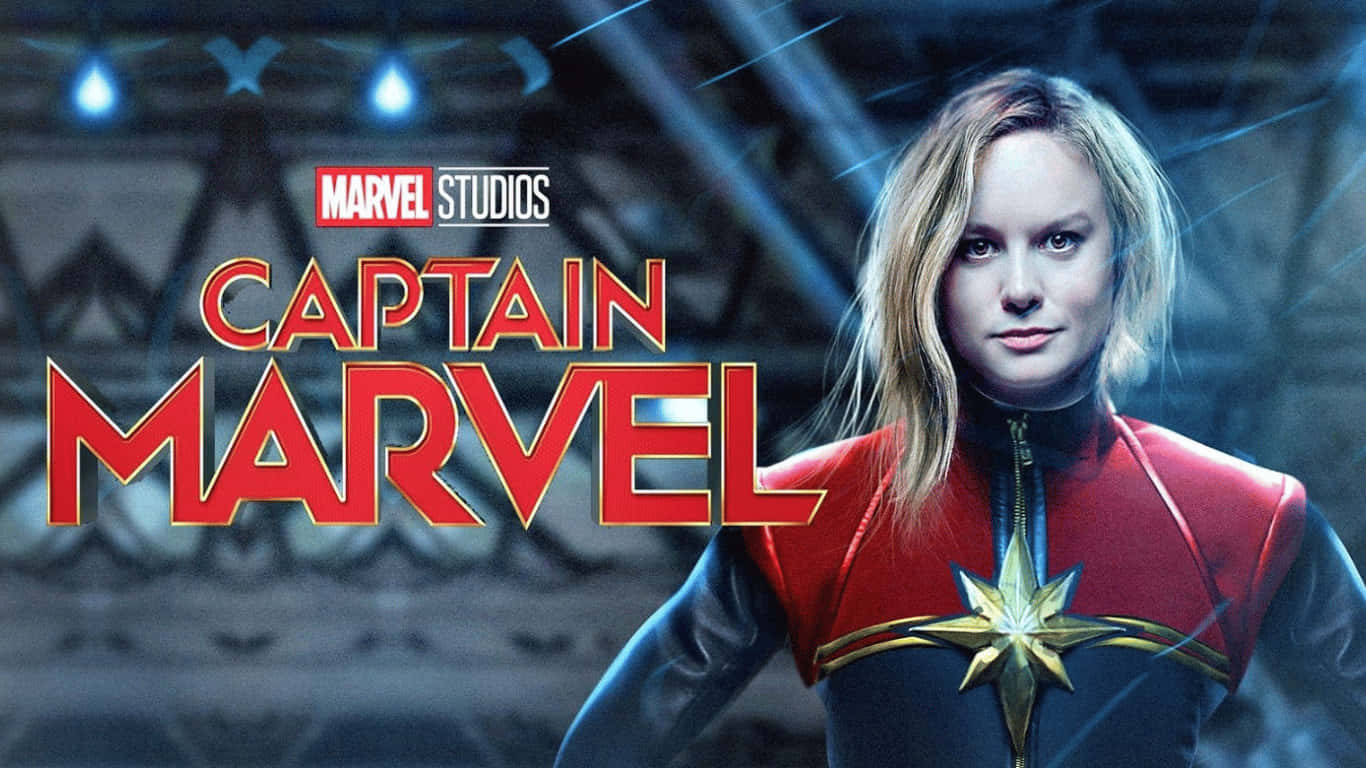 Hero 桌布 壁紙 — Captain Marvel 自信地站在她的紅藍戰衣中，胸前閃耀的星星標誌襯托著未來感的金屬背景。