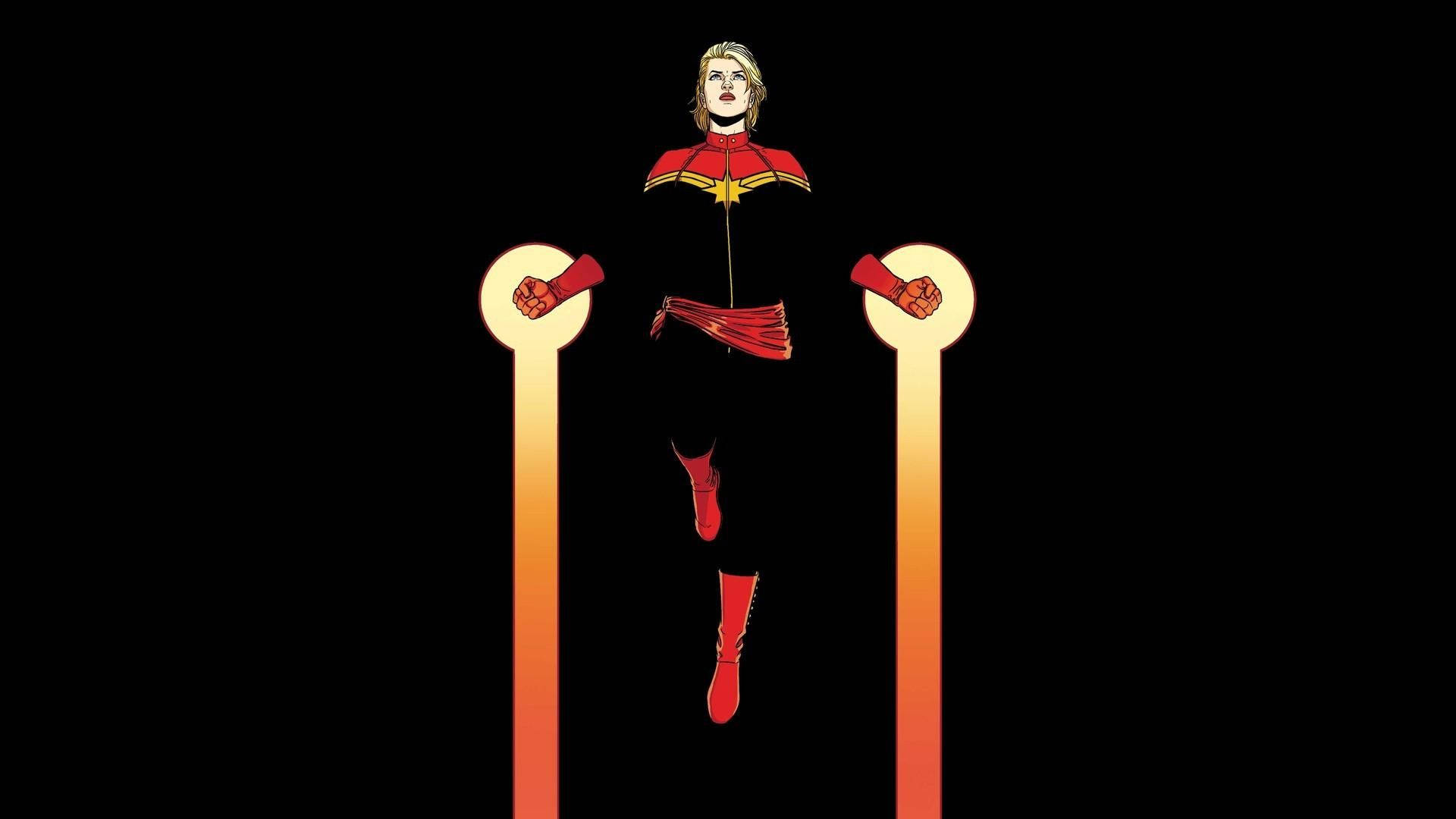 Captain Marvel 桌布 壁紙 — Captain Marvel 英雄地站在兩根發光的橙色柱子之間，背景為黑色。
