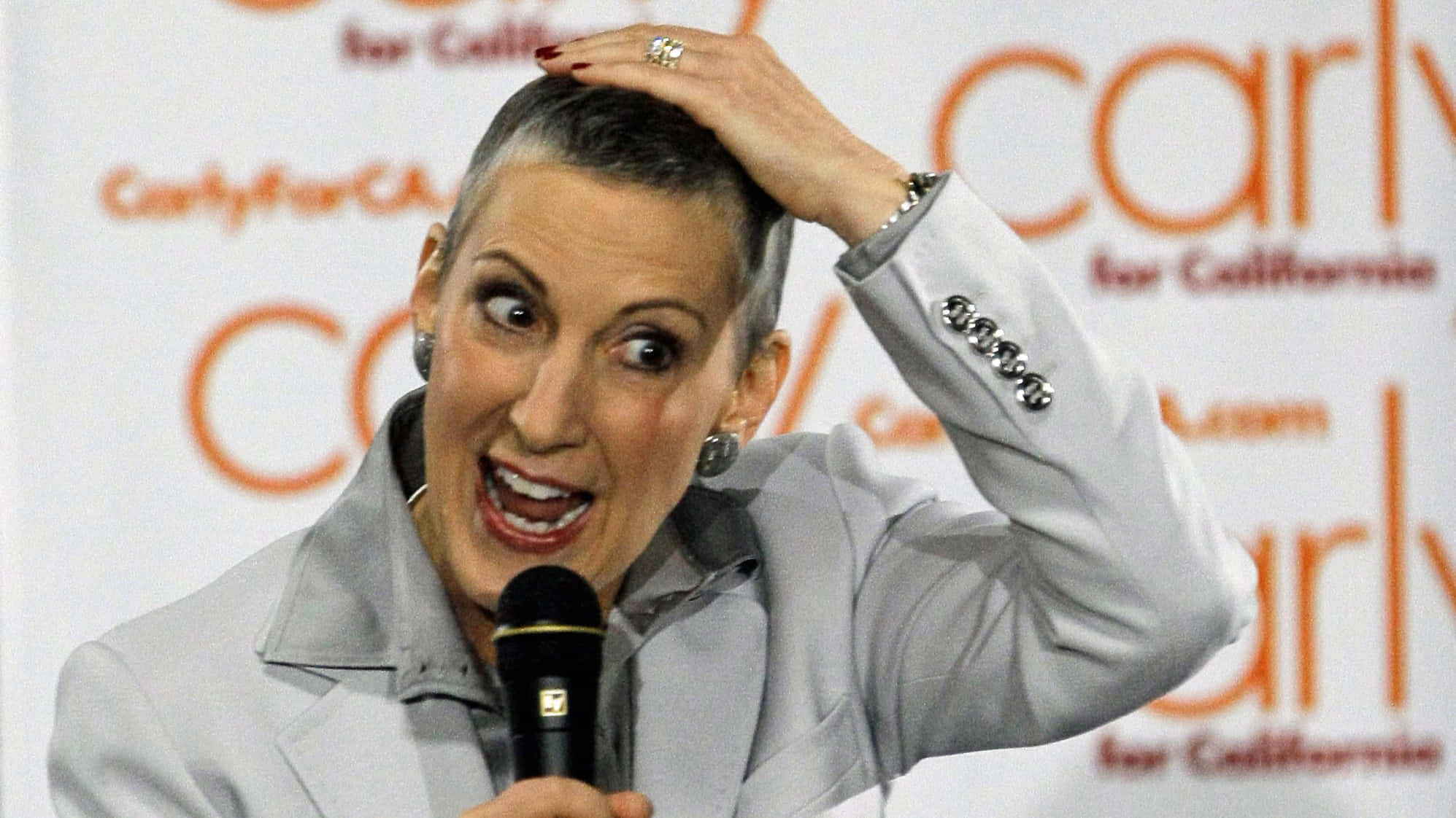 政治 桌布 壁紙 — Carly Fiorina 熱情地對著麥克風說話，一手放在頭上，背景是競選活動。